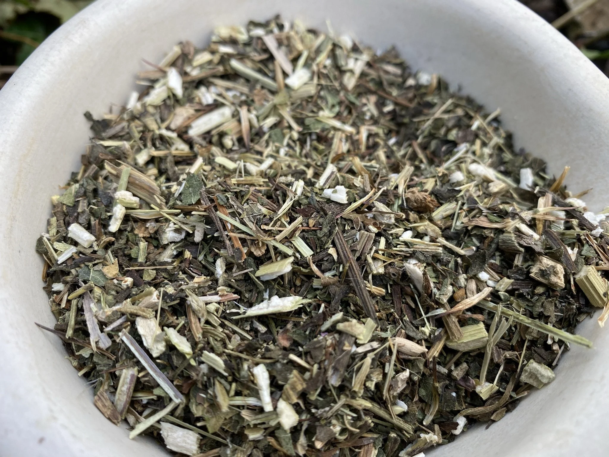 A white bowl filled with dried, crushed herbs and plant materials.
