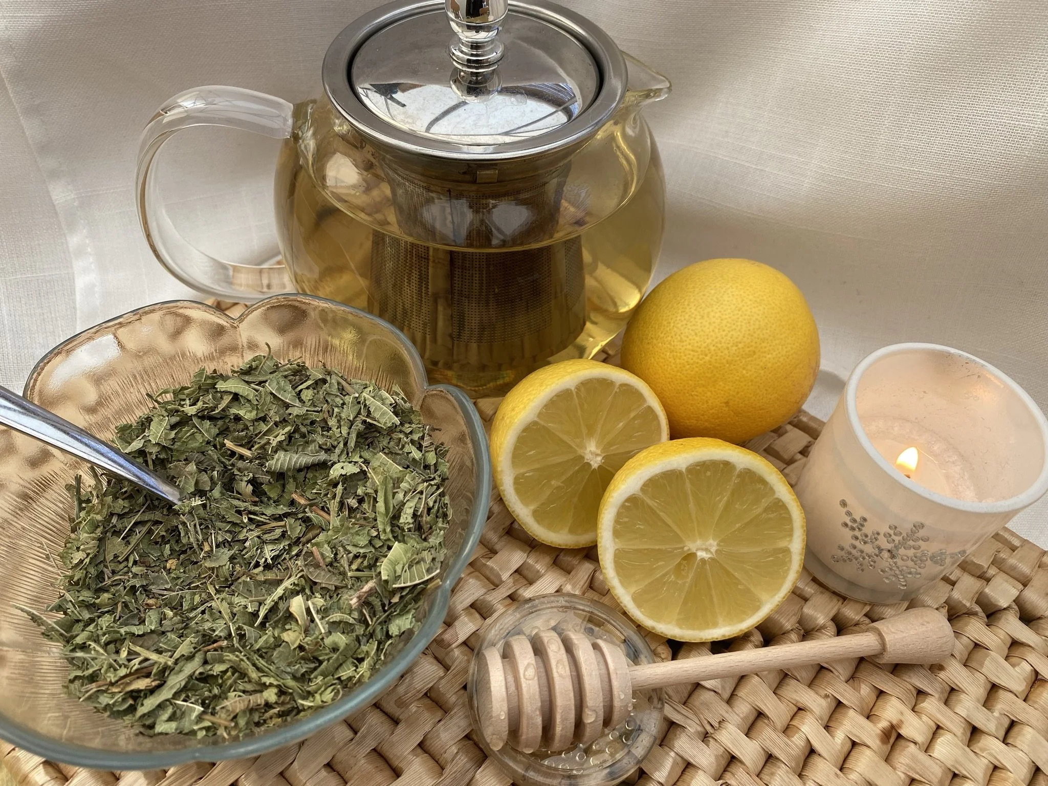 Glass teapot of brewed Lemon Verbena herbal tea with fresh lemon and honey on a woven mat
