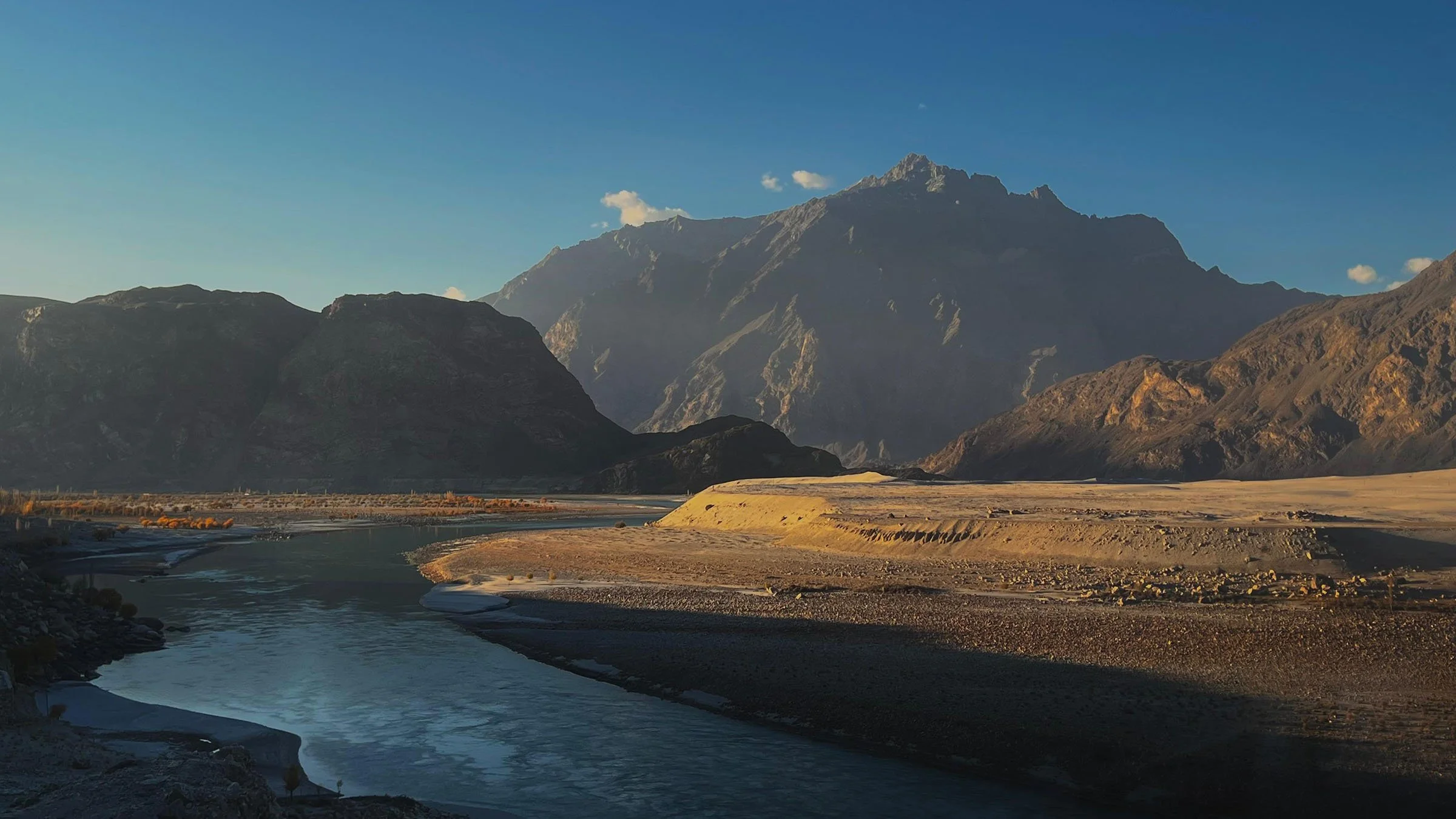 Scenic view of a river flowing through a valley with mountains in the background under a clear blue sky.