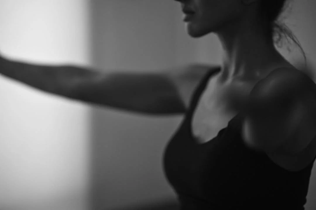 A black and white photo of a woman in a tank top stretching her arms.