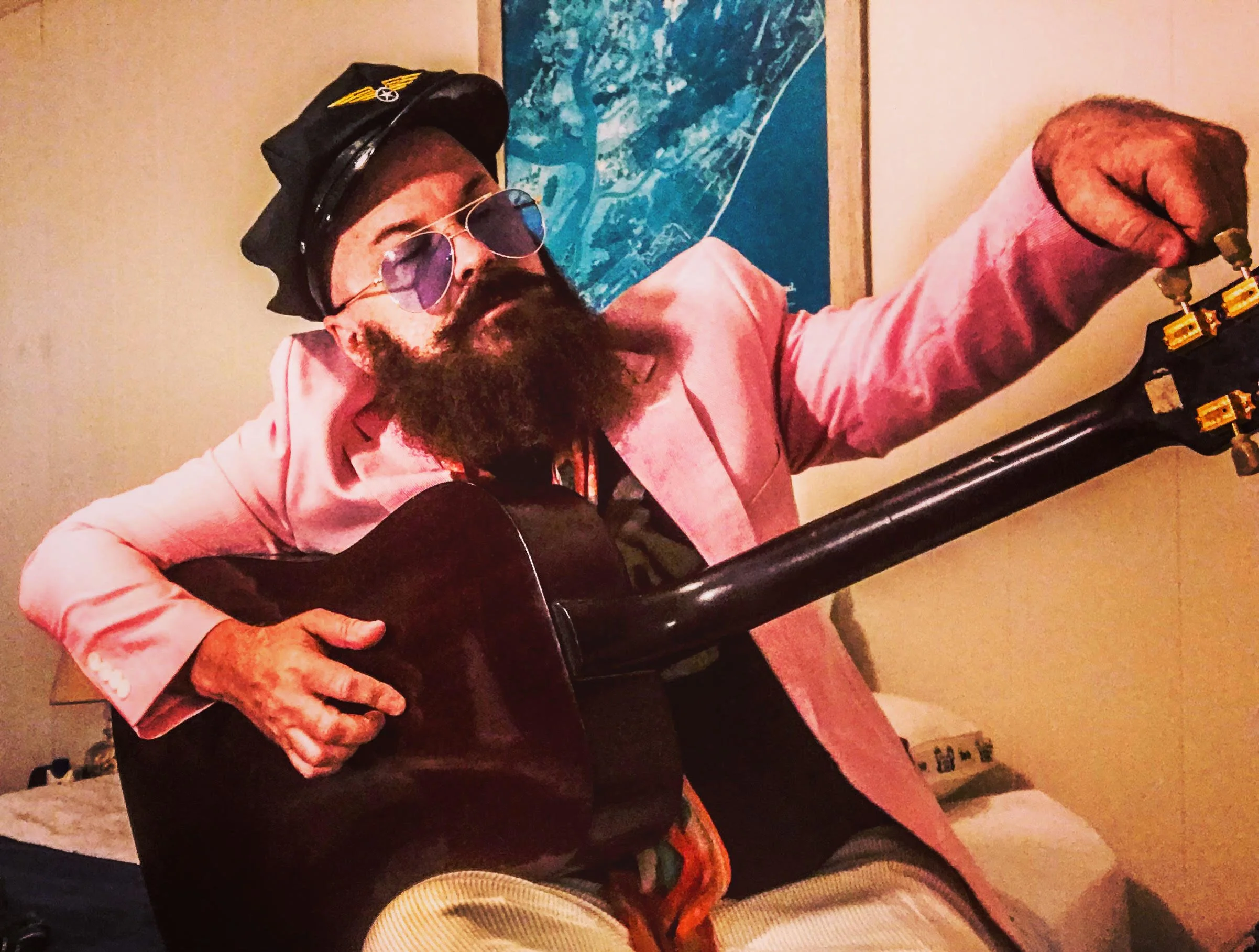 Photo of Angie Aparo running a guitar wearing a pink suit jacket and a pilot cap.