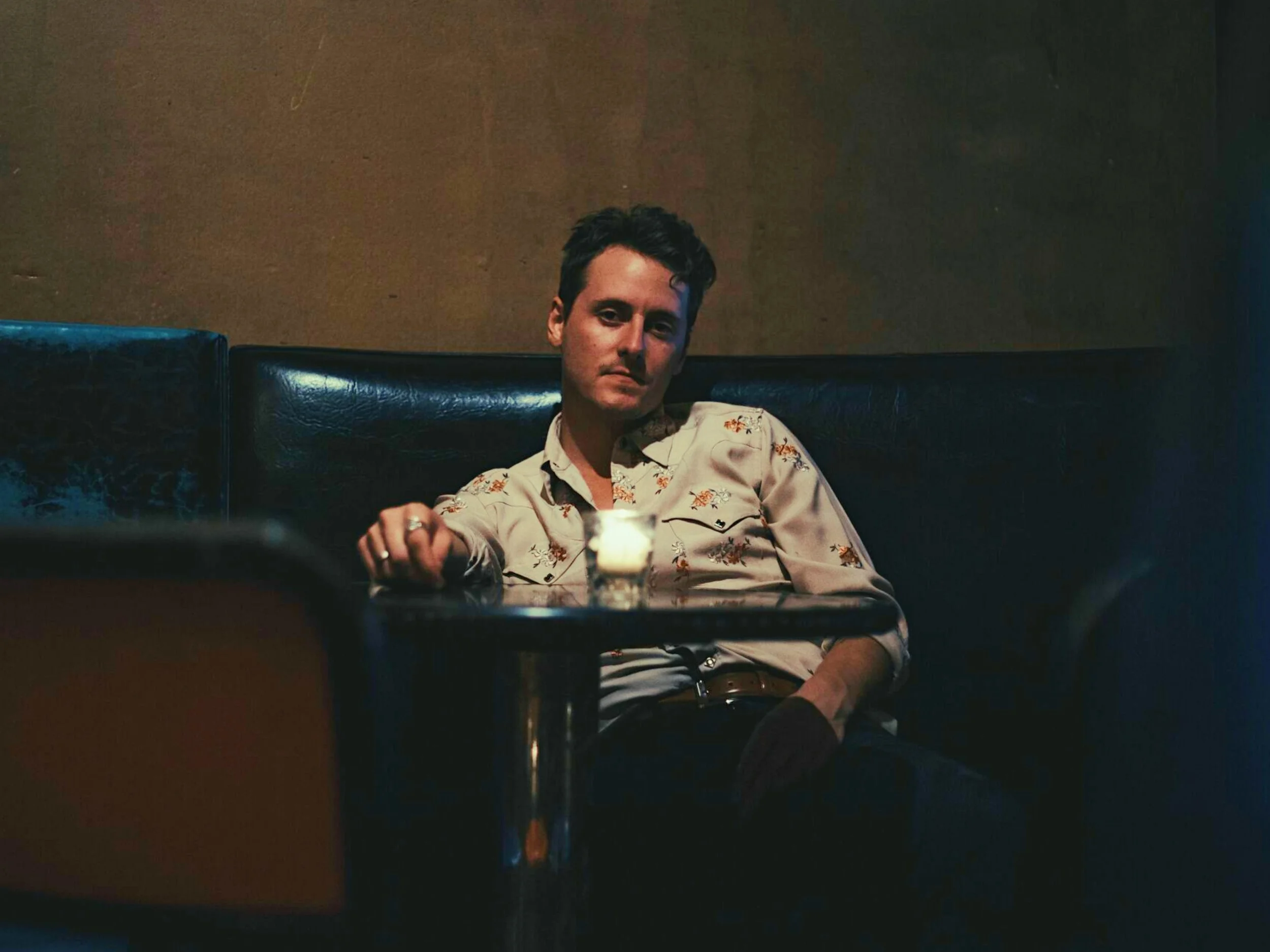 Austin Plaine sits in a blue booth behind a table in a flower design button up shirt.