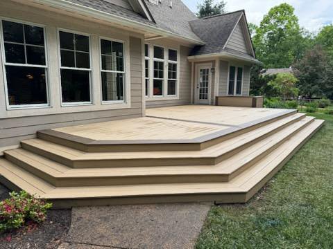 Newly built, multi-level wooden deck attached to the back of a house, with steps leading down to a grass yard.