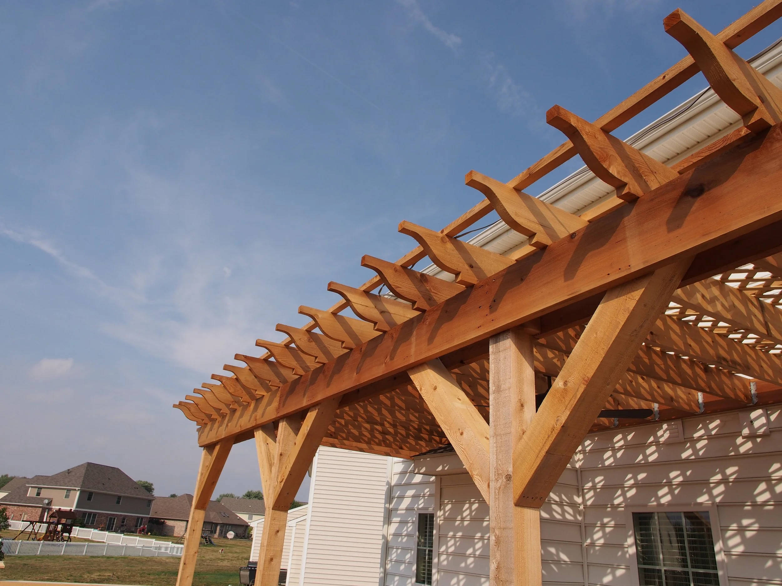 Wooden pergola structure under construction in a backyard with neighboring houses and blue sky.