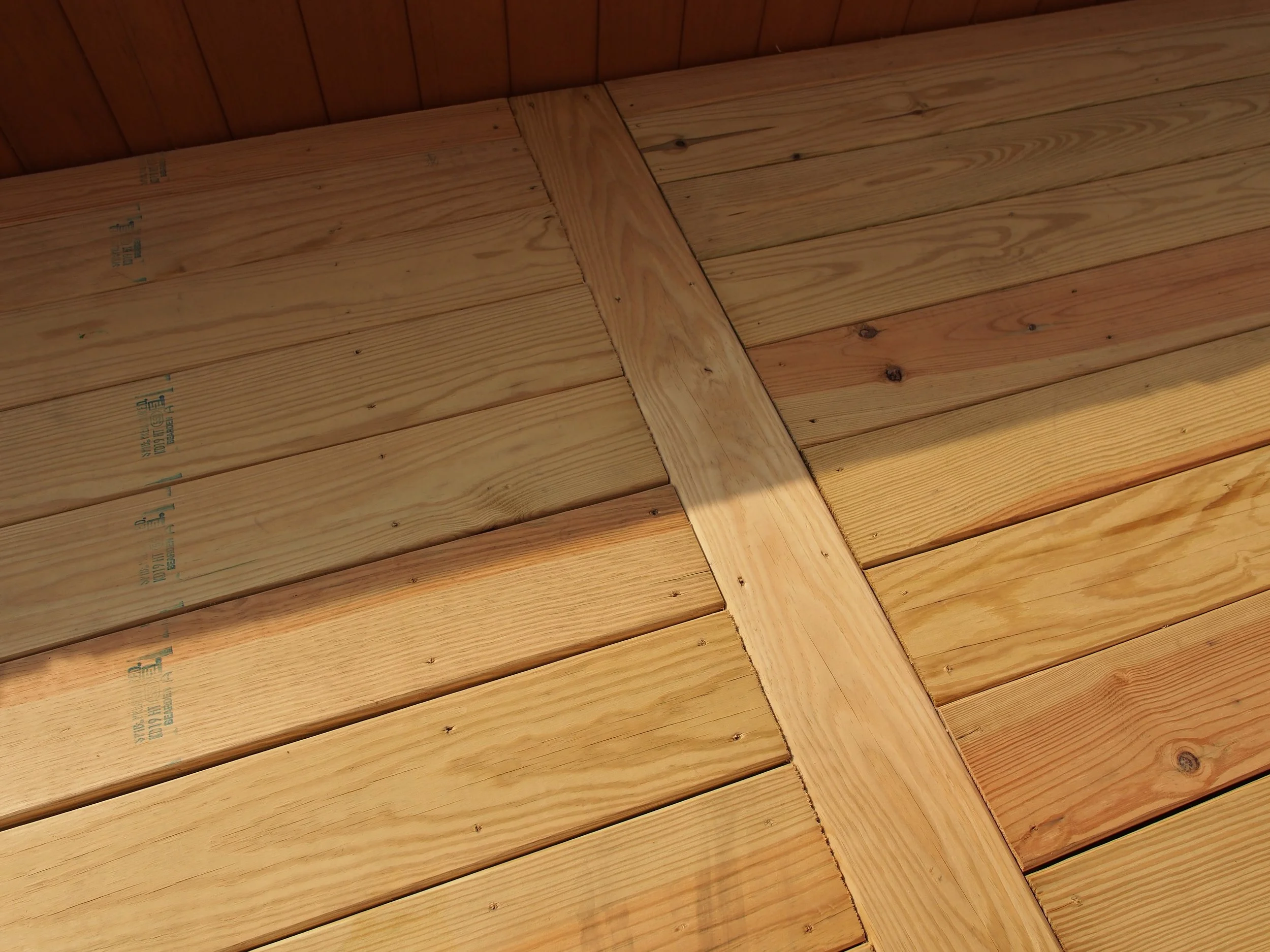 Close-up of a wooden ceiling with natural wood planks and a crossbeam, showing the wood grain and nails.