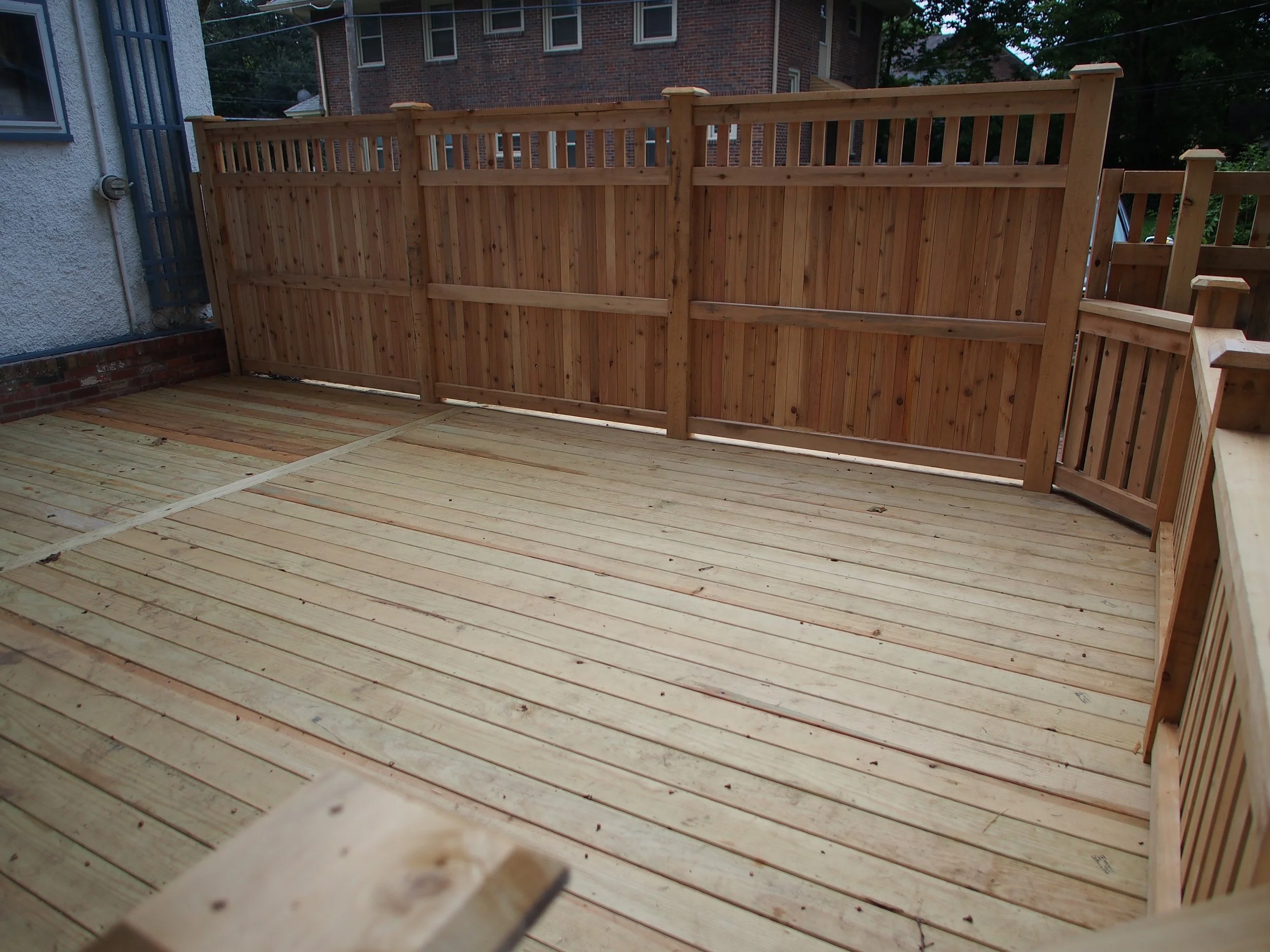 A freshly constructed wooden deck with a wooden fence around it, attached to a residential building.