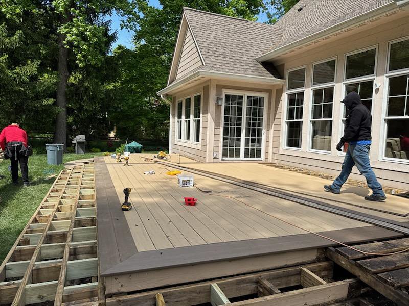 Construction workers are installing a new deck on the back of a house, with tools and materials scattered around.