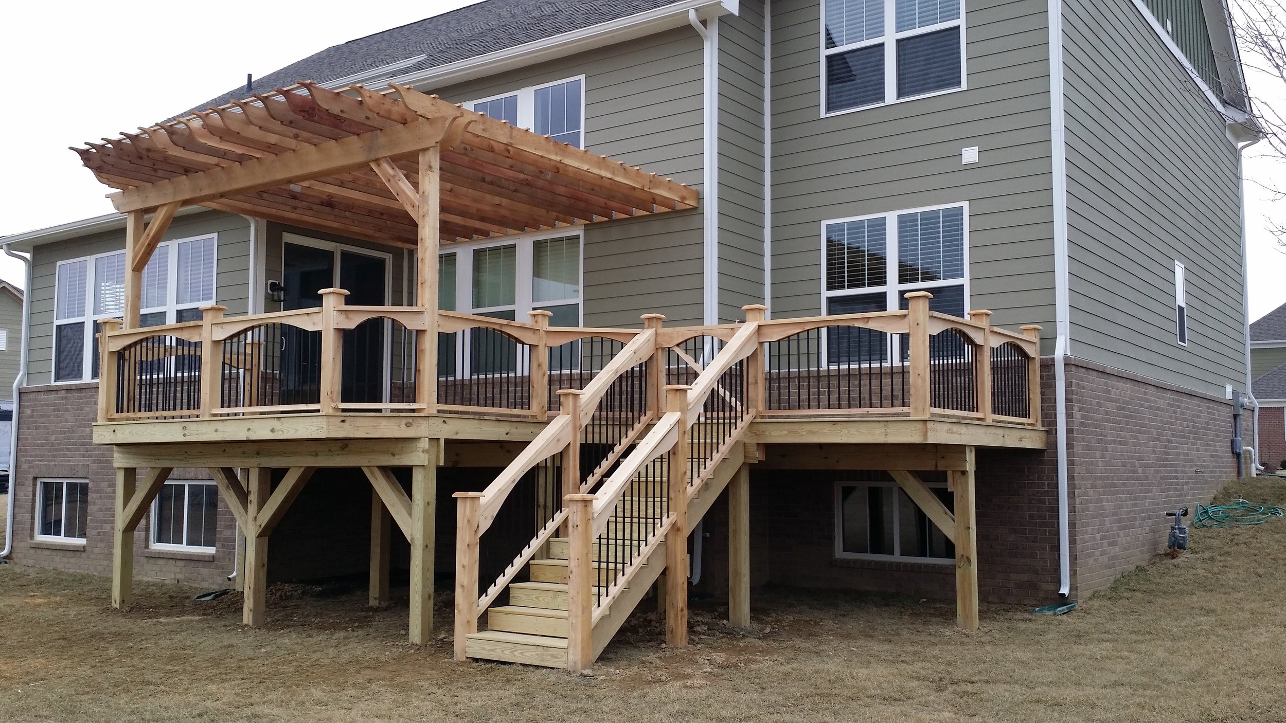 A newly constructed wooden deck with staircase and black metal railing attached to a tan-colored house with multiple windows.