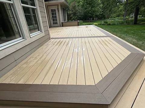 Close-up view of a wooden deck attached to a house, with a beige and gray color scheme, surrounded by a grassy yard.
