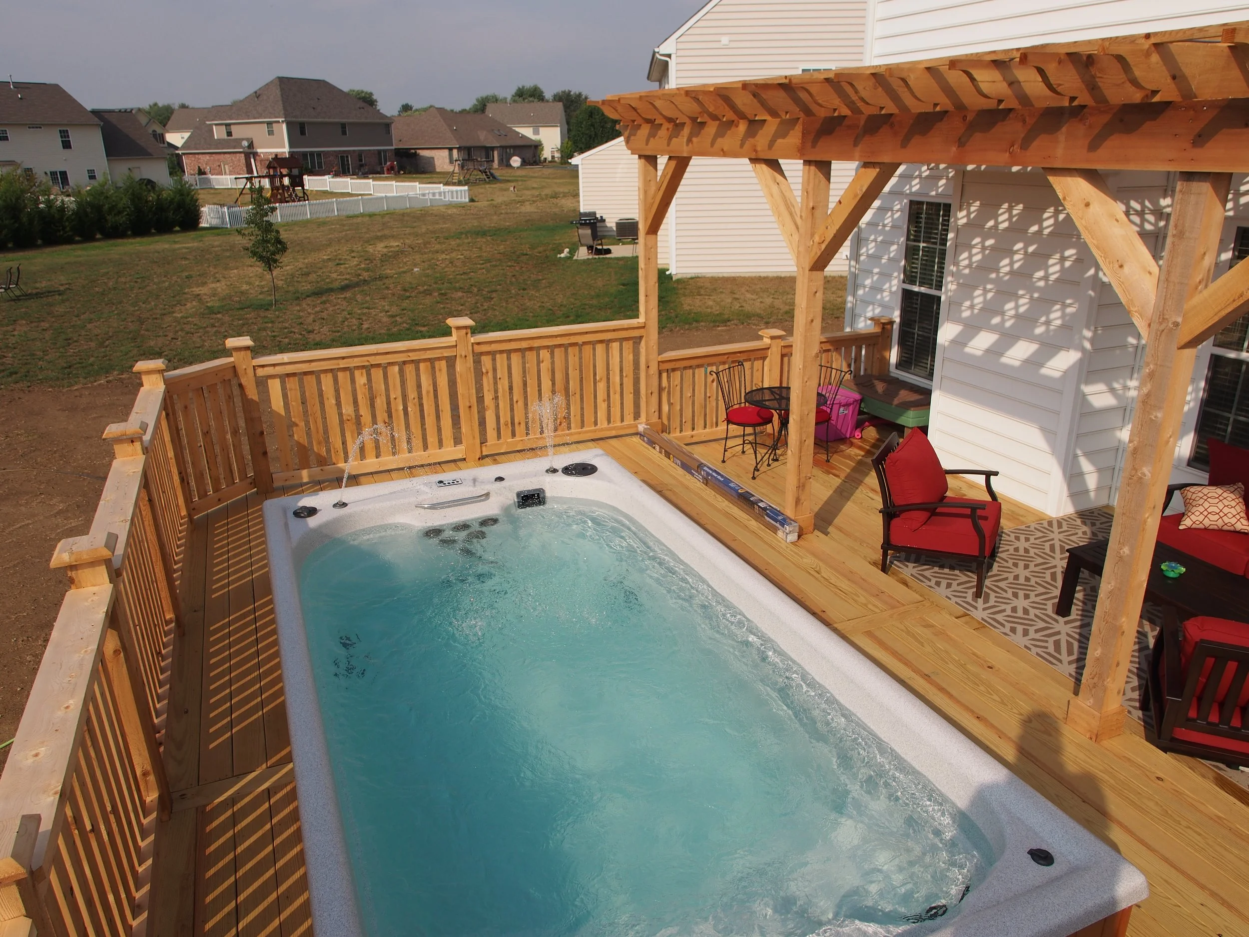 Backyard with a wooden deck, hot tub, patio furniture, and neighboring houses in the background.