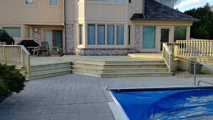 Home exterior with a wooden deck, stairs, and a swimming pool covered with a blue pool cover.