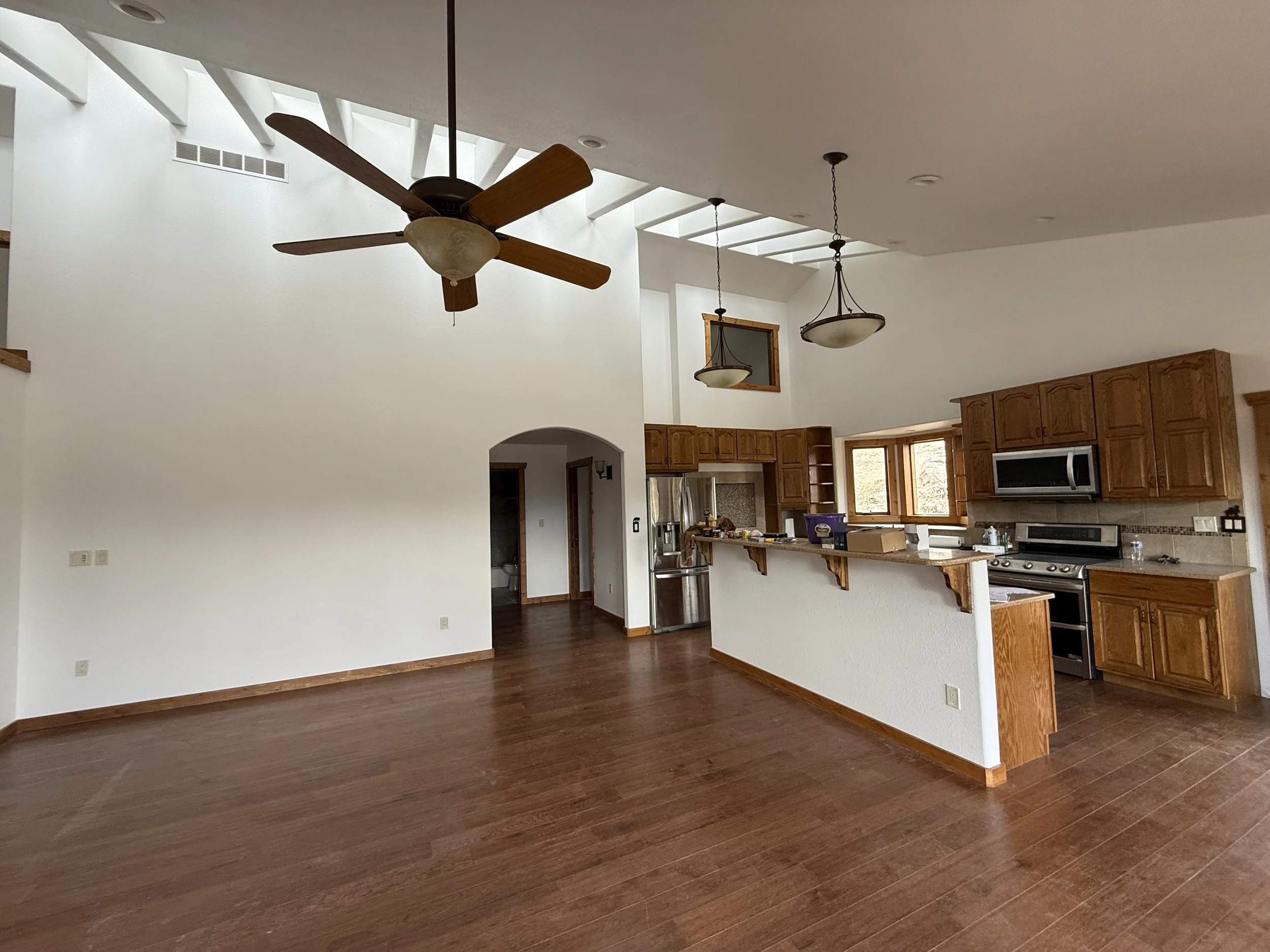 Open-concept kitchen and living space with wood floors, kitchen cabinets, and ceiling fans.