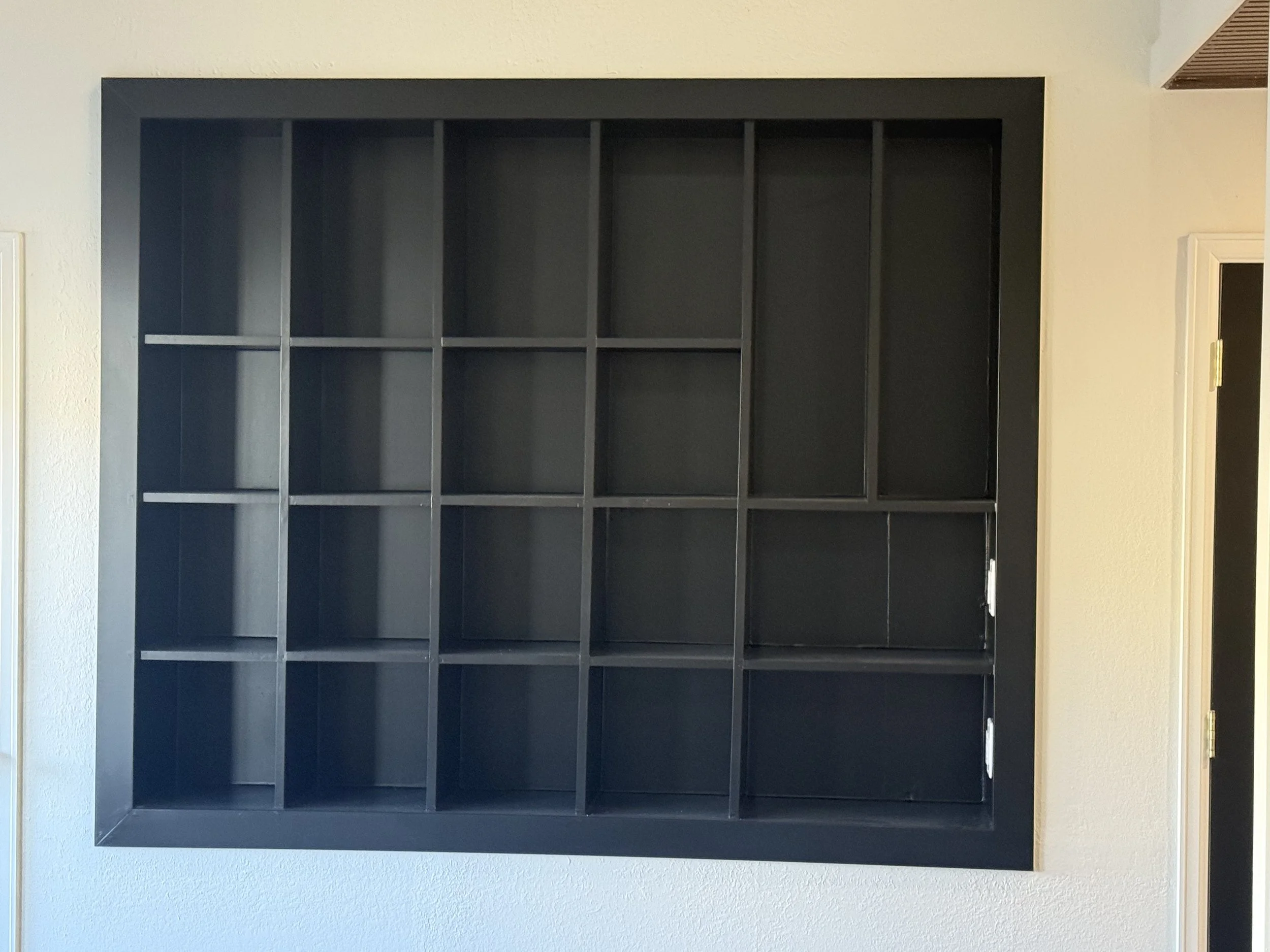 Large black wall-mounted shelving unit with multiple empty compartments against a light-colored wall.