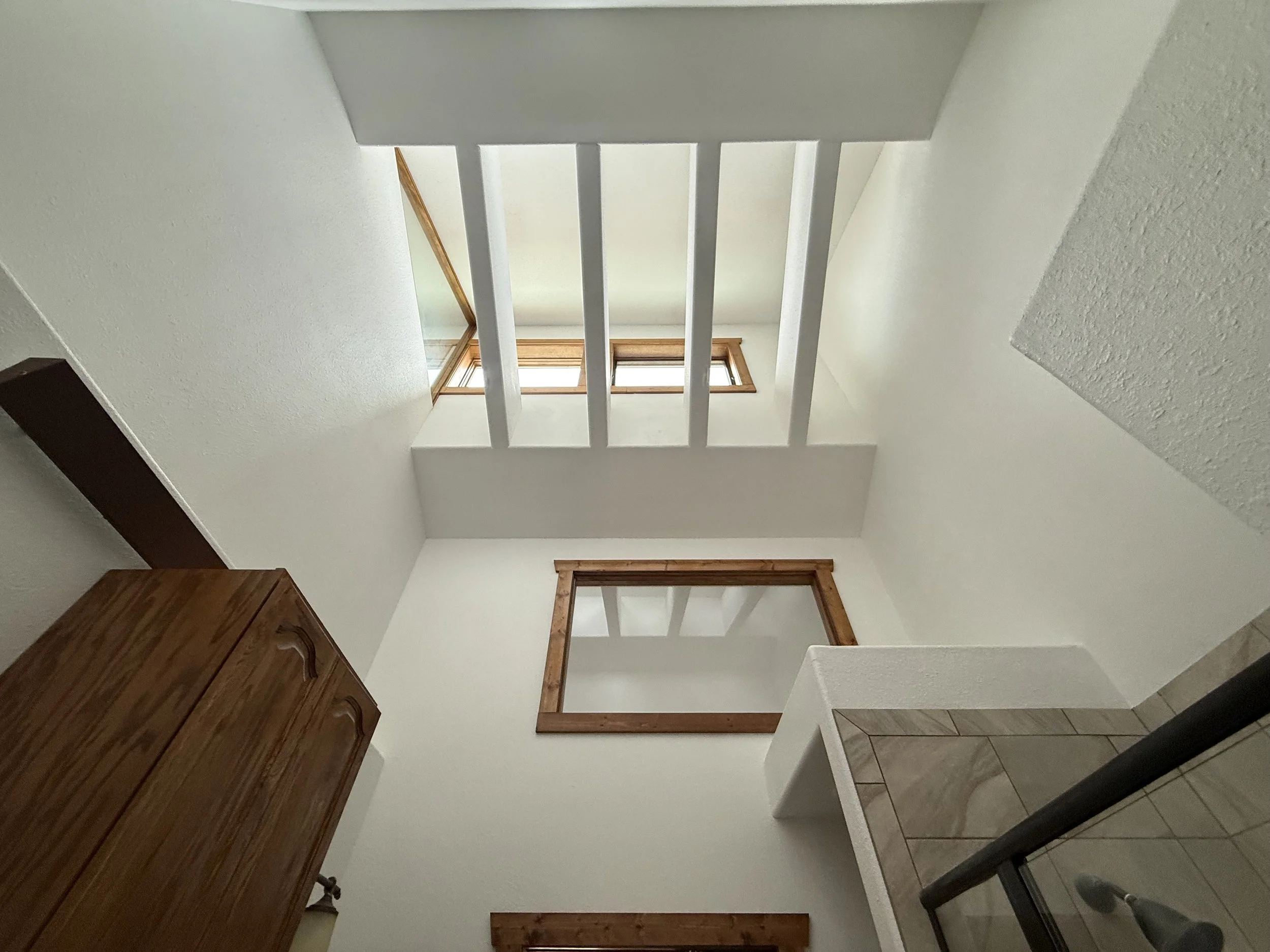 View looking up at the ceiling of a small room with a skylight window. The room has white walls, wooden trim around the window and a large wooden cabinet on the left side.