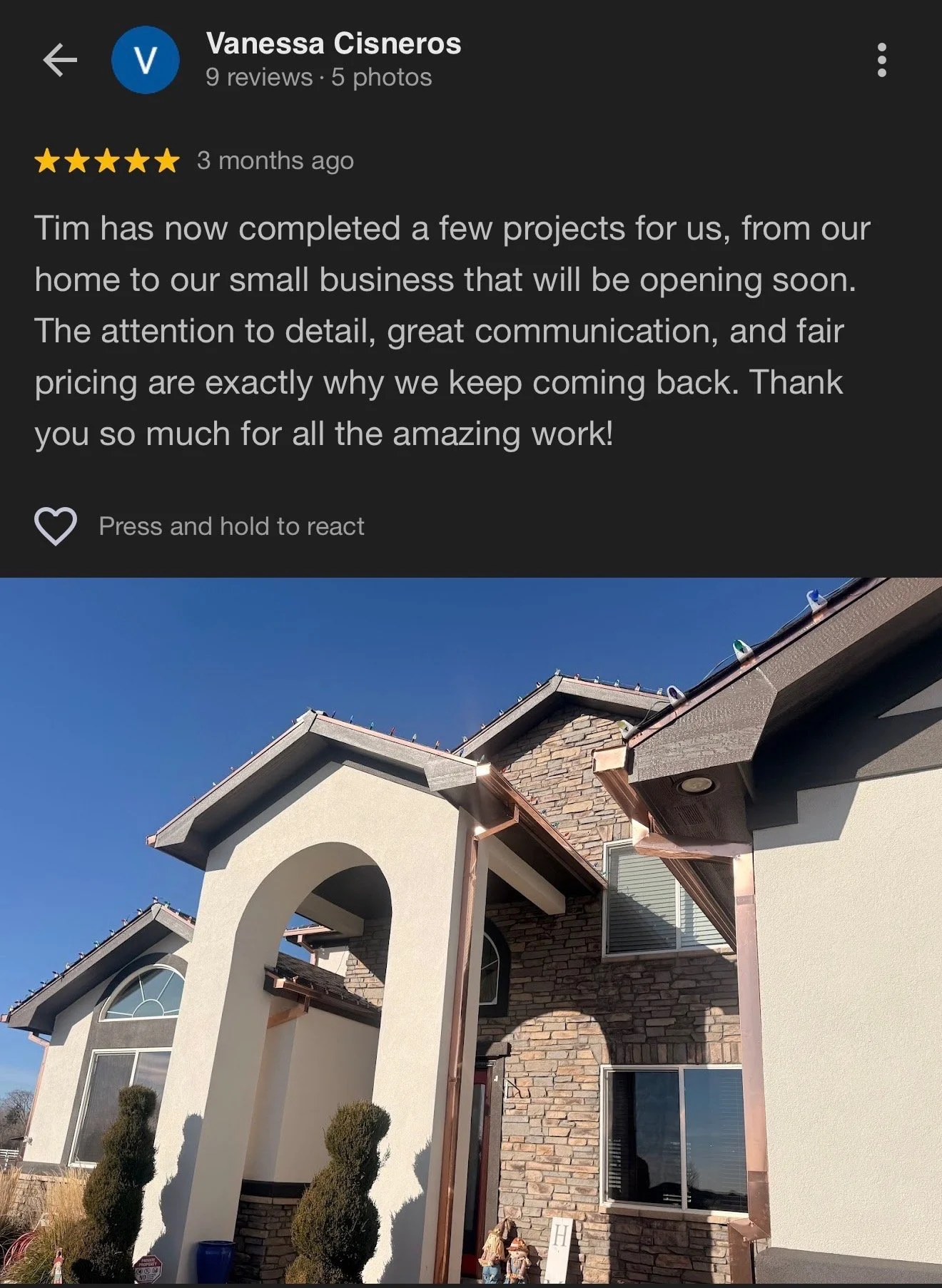 Exterior view of a house with a combination of stone and stucco siding, arched entryway, and brown roof shingles, under a clear blue sky.
