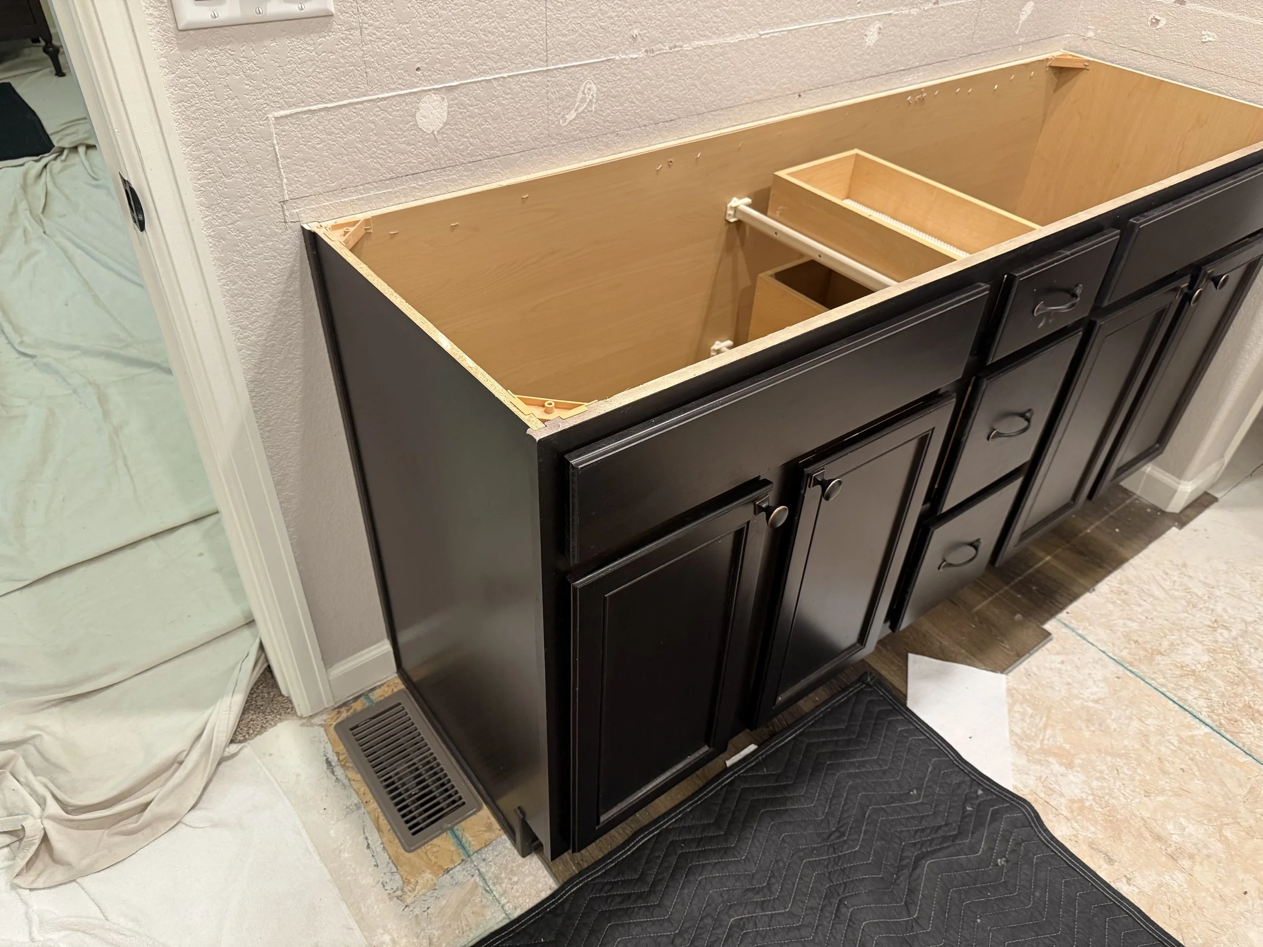 Kitchen cabinet under renovation with open top drawers and shelves, black exterior, beige interior, and partially installed hardware.