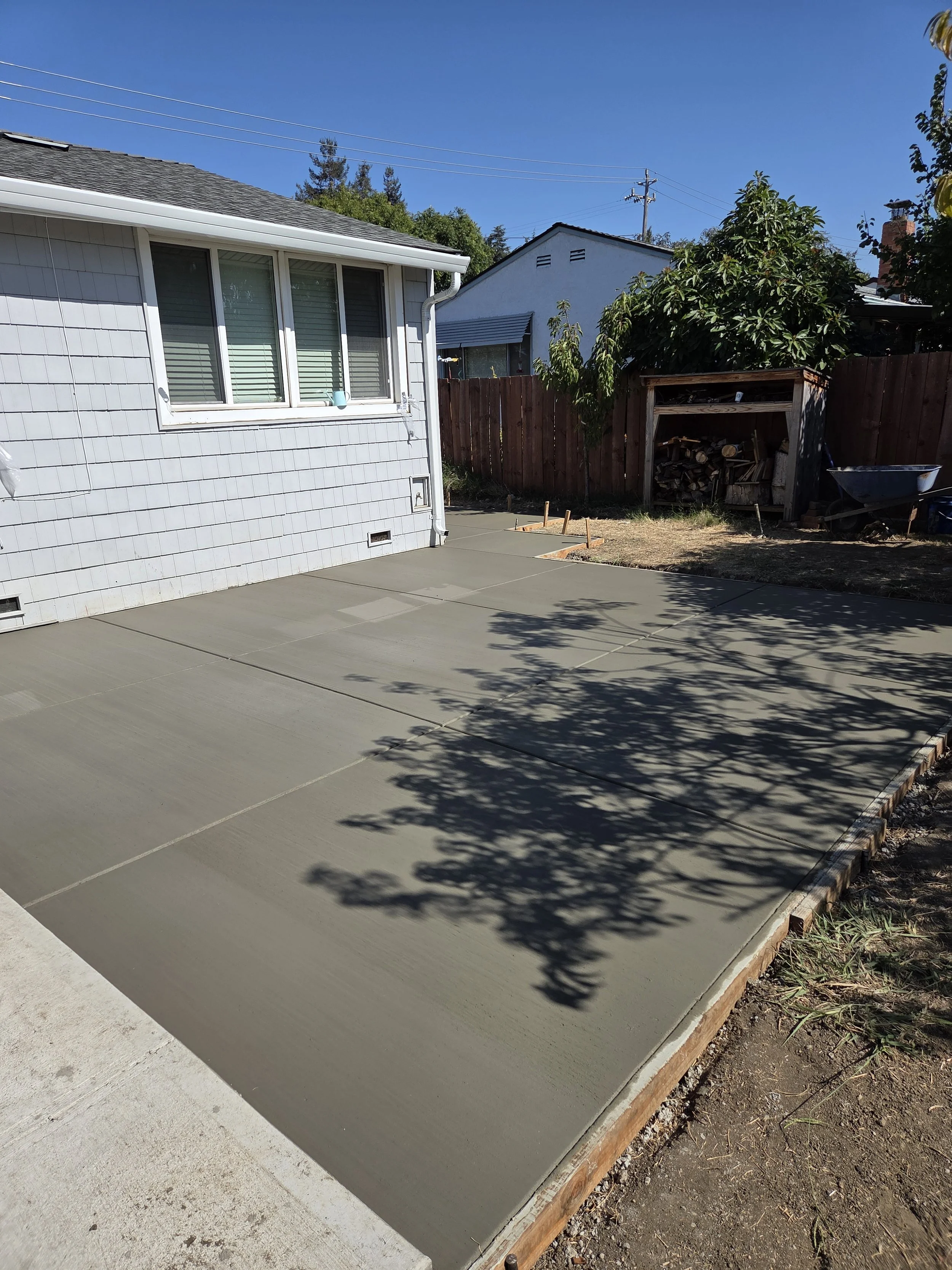 Freshly poured concrete on a backyard patio with shadow of a tree.
