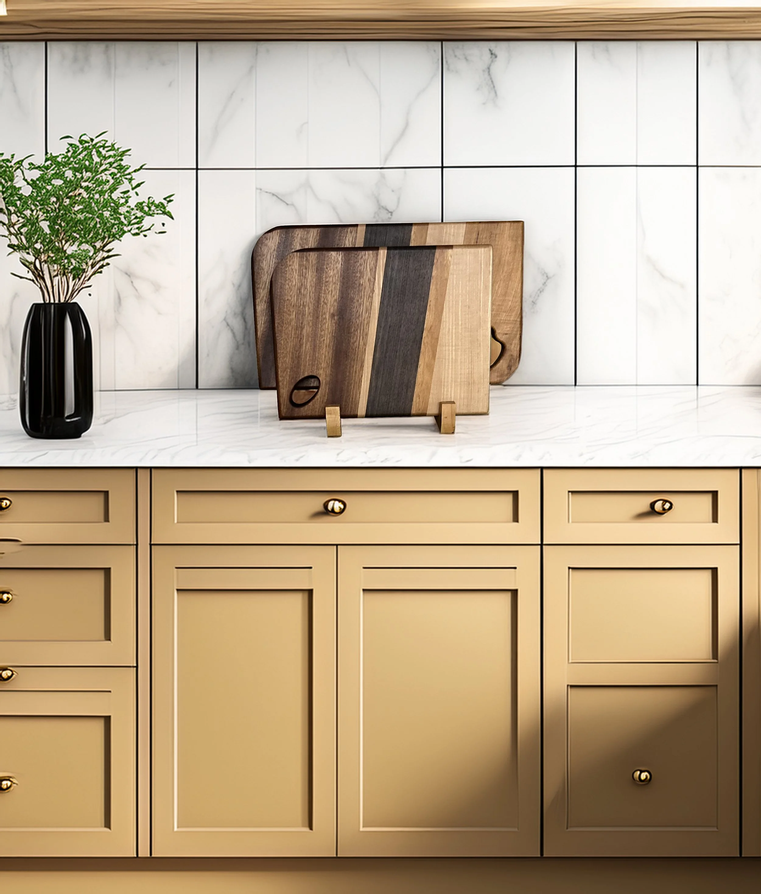 Kitchen counter with three wooden cutting boards leaning against a white marble backsplash wall. A black vase with green plants is on the left. The kitchen cabinets are painted yellow with black and gold knobs.