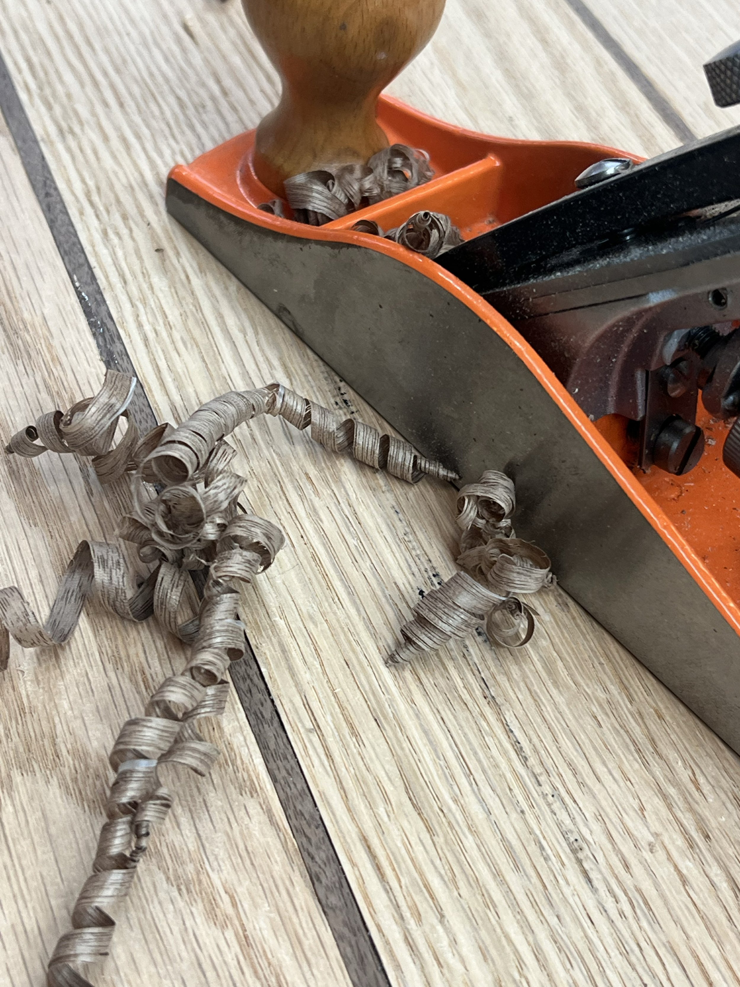 Wood shavings on a floor near a hand planer tool.