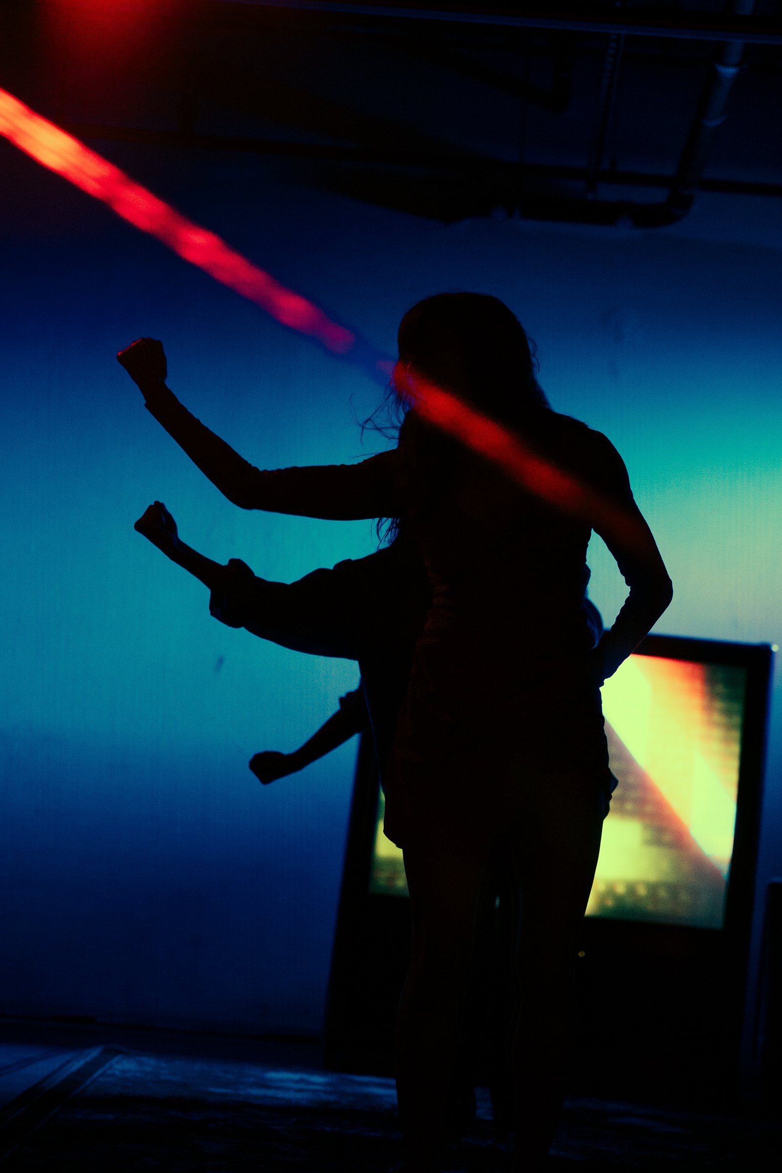 Silhouettes of people dancing with colorful lights and a digital screen in the background.