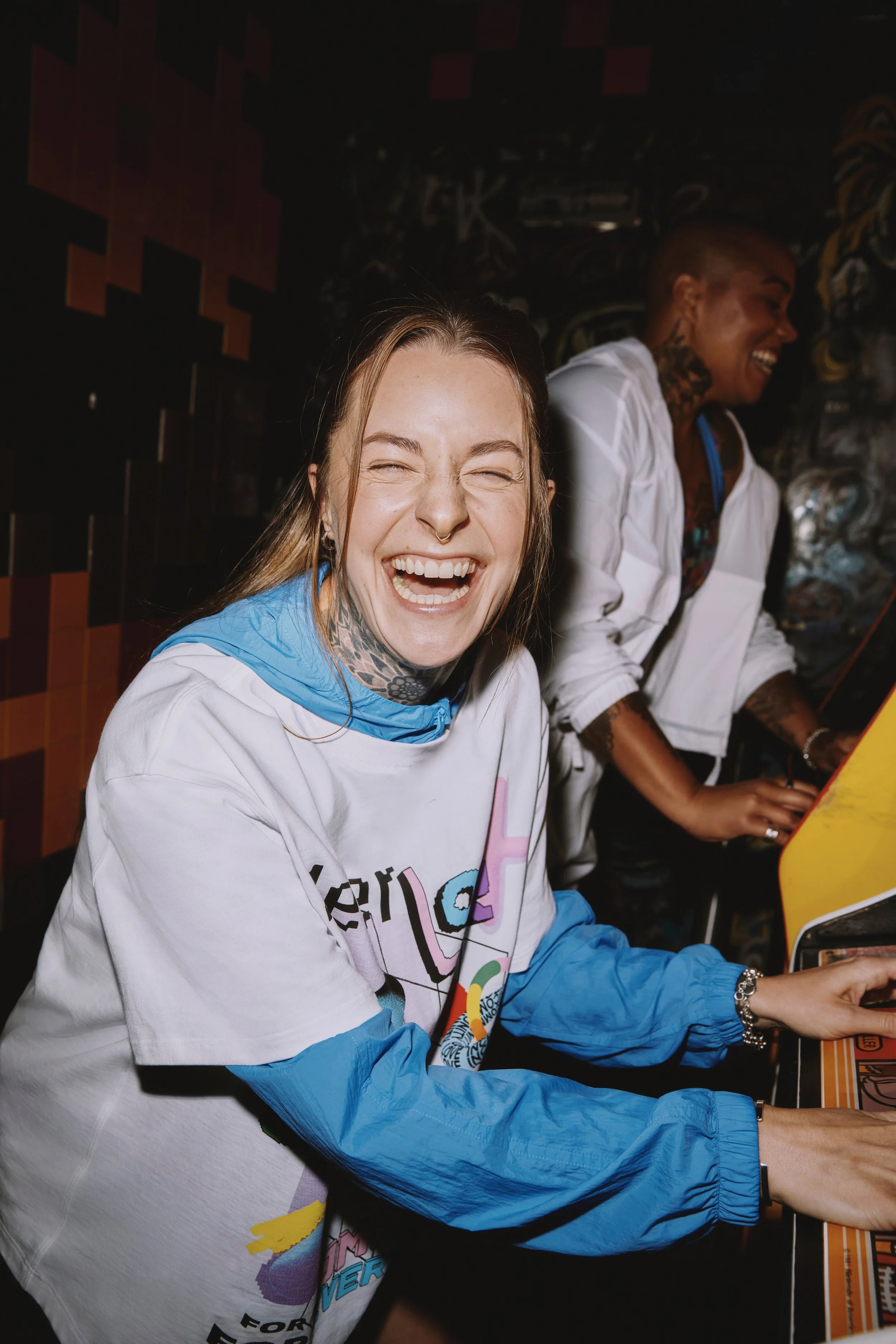 Two people playing arcade video games and laughing.