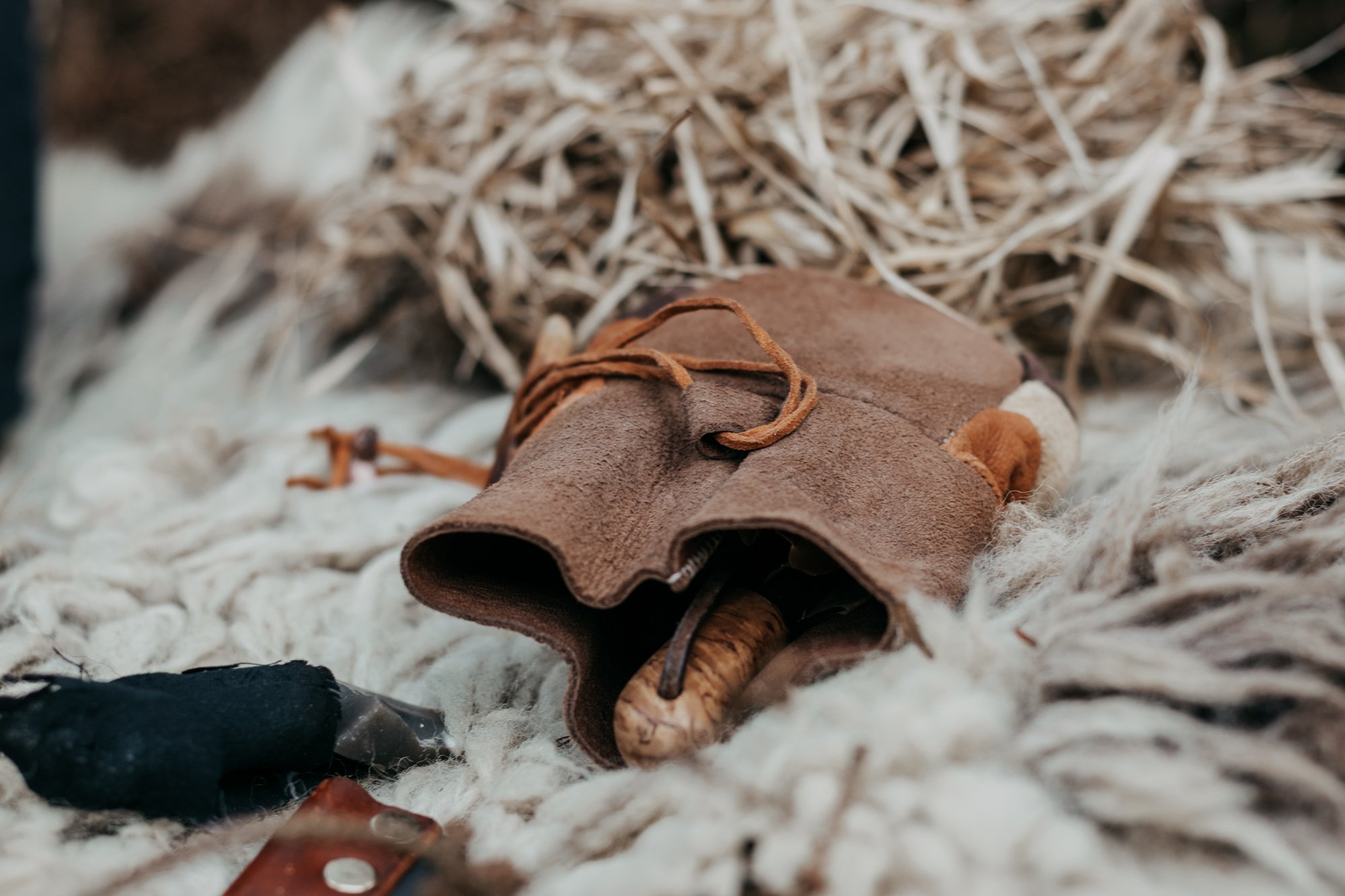A pair of brown leather gloves resting on a cream-colored wool blanket with straw in the background.
