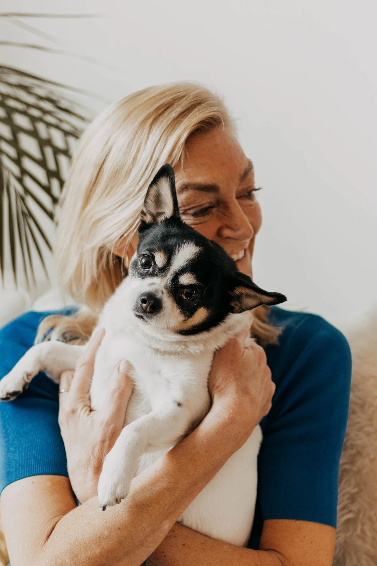 A woman with blonde hair smiling and hugging a small black and white dog.