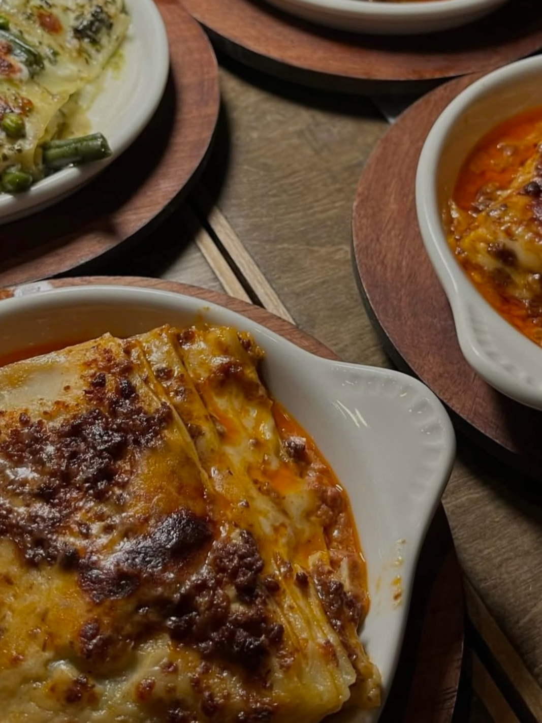 Baked lasagna with melted cheese and ground meat, served in a white dish on a wooden tray.