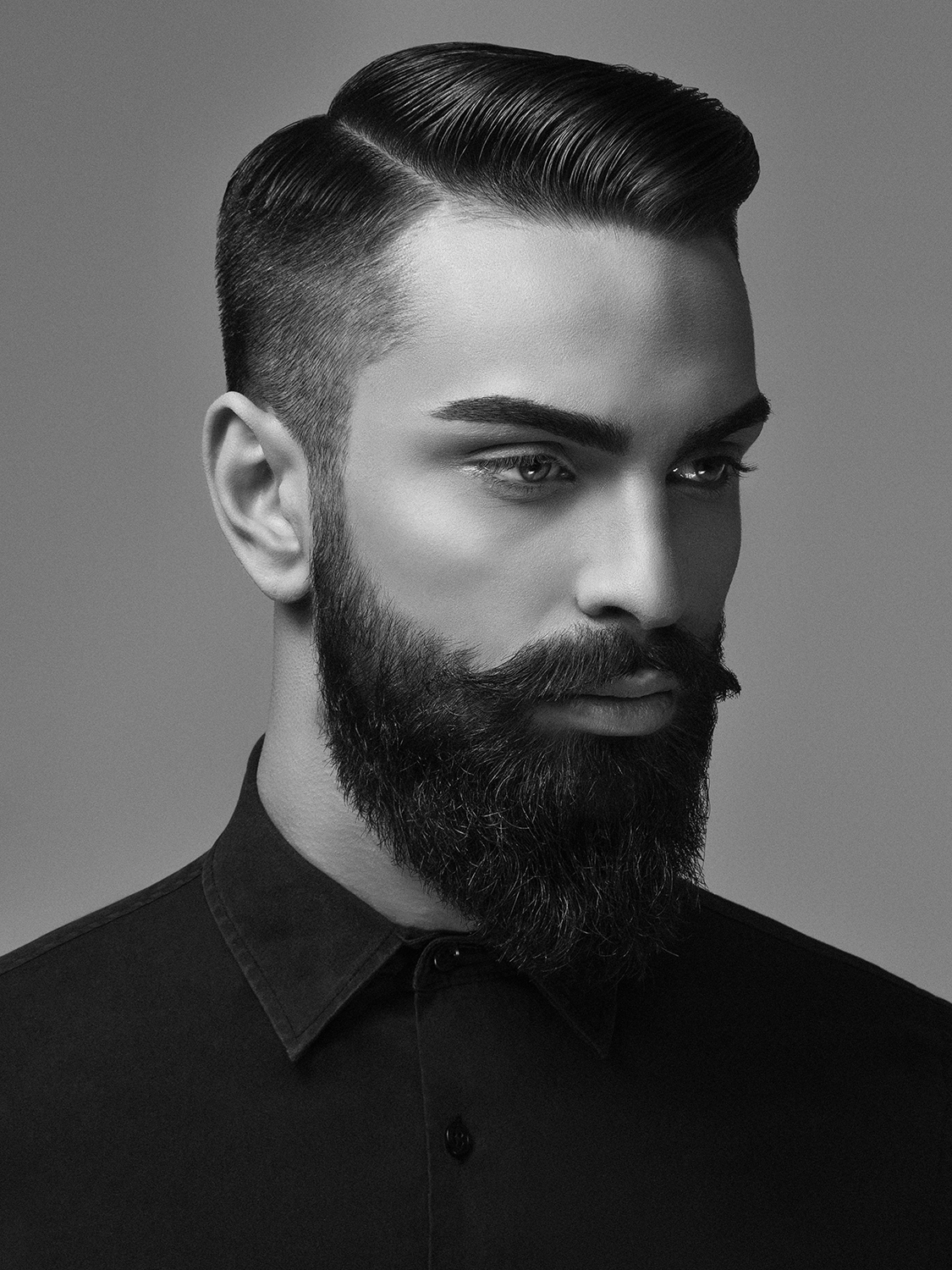 Black and white portrait of a man with styled hair, a full beard, and mustache, wearing a collared shirt.