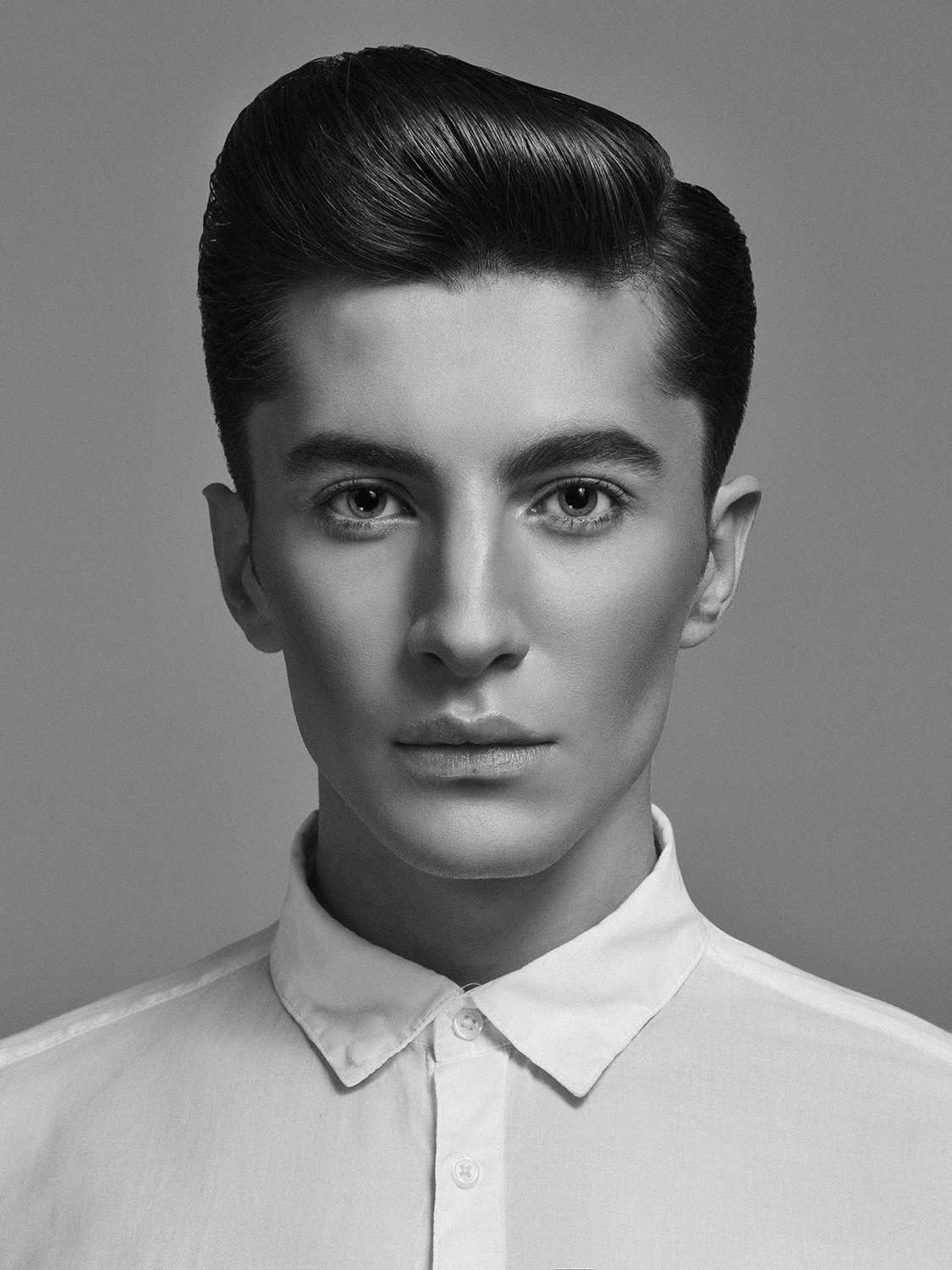 Black and white portrait of a woman with slicked-back hair, wearing a collared shirt against a plain background.