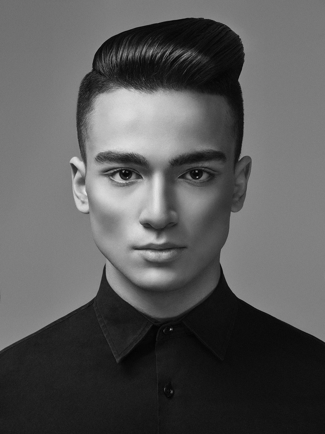 Black and white portrait of a young man with styled hair, wearing a collared shirt, looking directly at the camera.