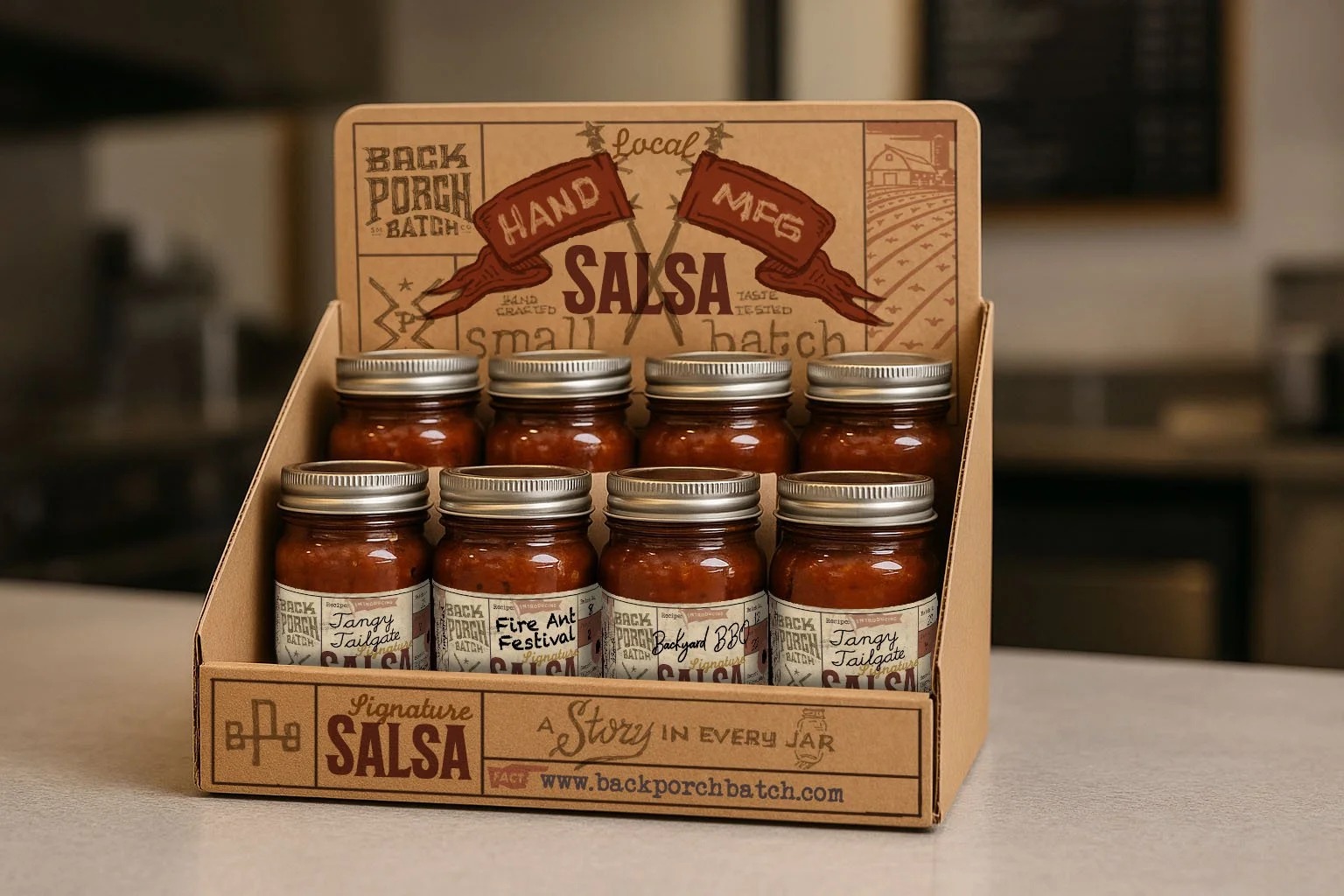A display of small jars of salsa in a cardboard box with a printed label. The label has the word 'Salsa' and features rustic, vintage-style graphics and text, including the website www.backporchbatch.com.