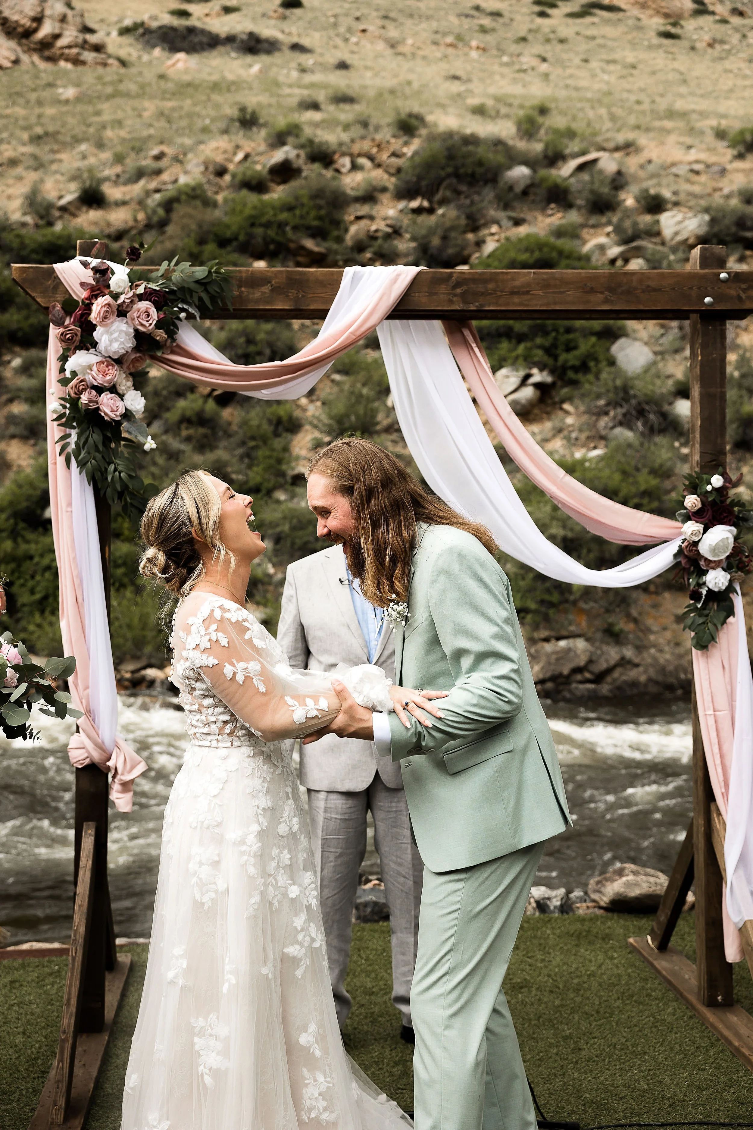 wedding couple laugh during a wedding ceremony with a rocky canyon backdrop and river