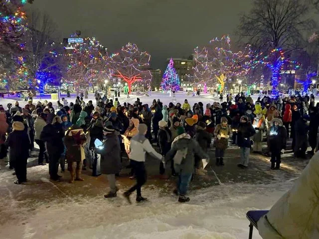 Mourners holding a candlelight vigil in a park lit with Christmas lights.