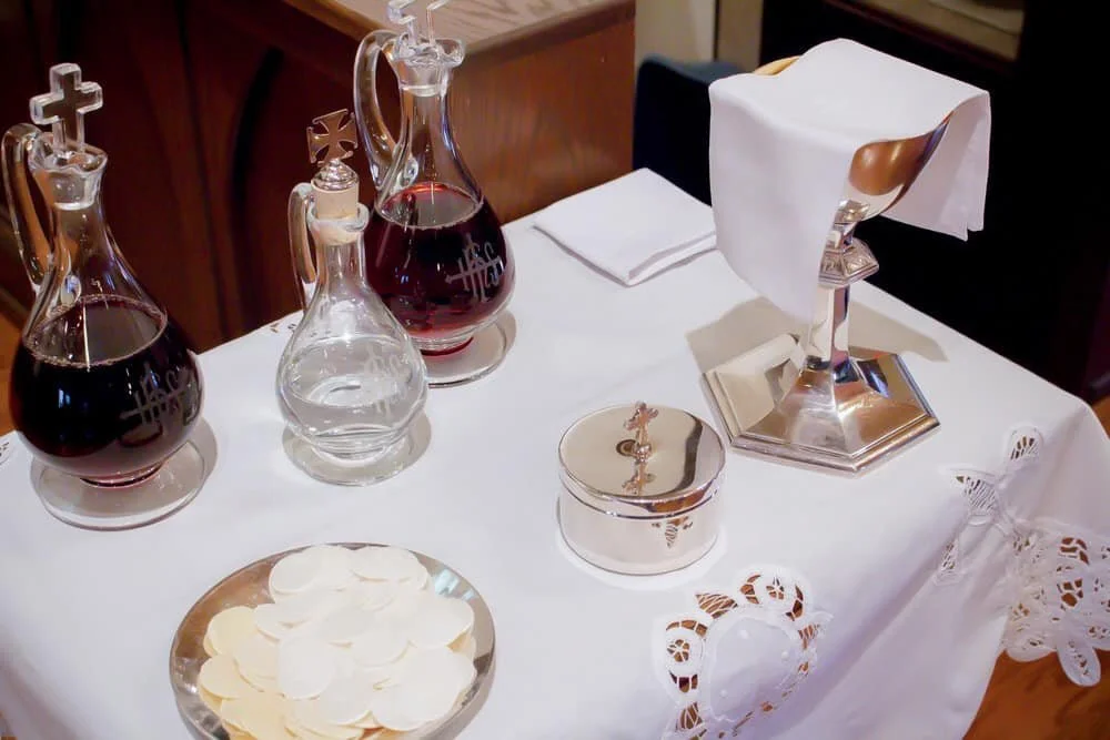 Religious table setup with glass decanters, a tissue holder, a plate of communion wafers, and a tablecloth with lace trim.
