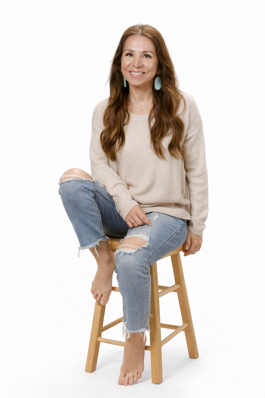 Portrait of a smiling woman with long brown hair, wearing a denim jacket and turquoise earrings, against a dark textured background.
