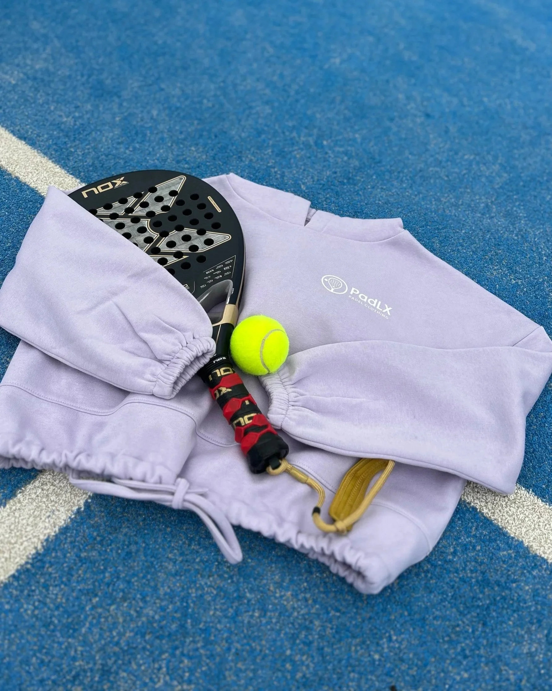 PadLX women’s cropped hoodie laid out on a padel court with racket and ball