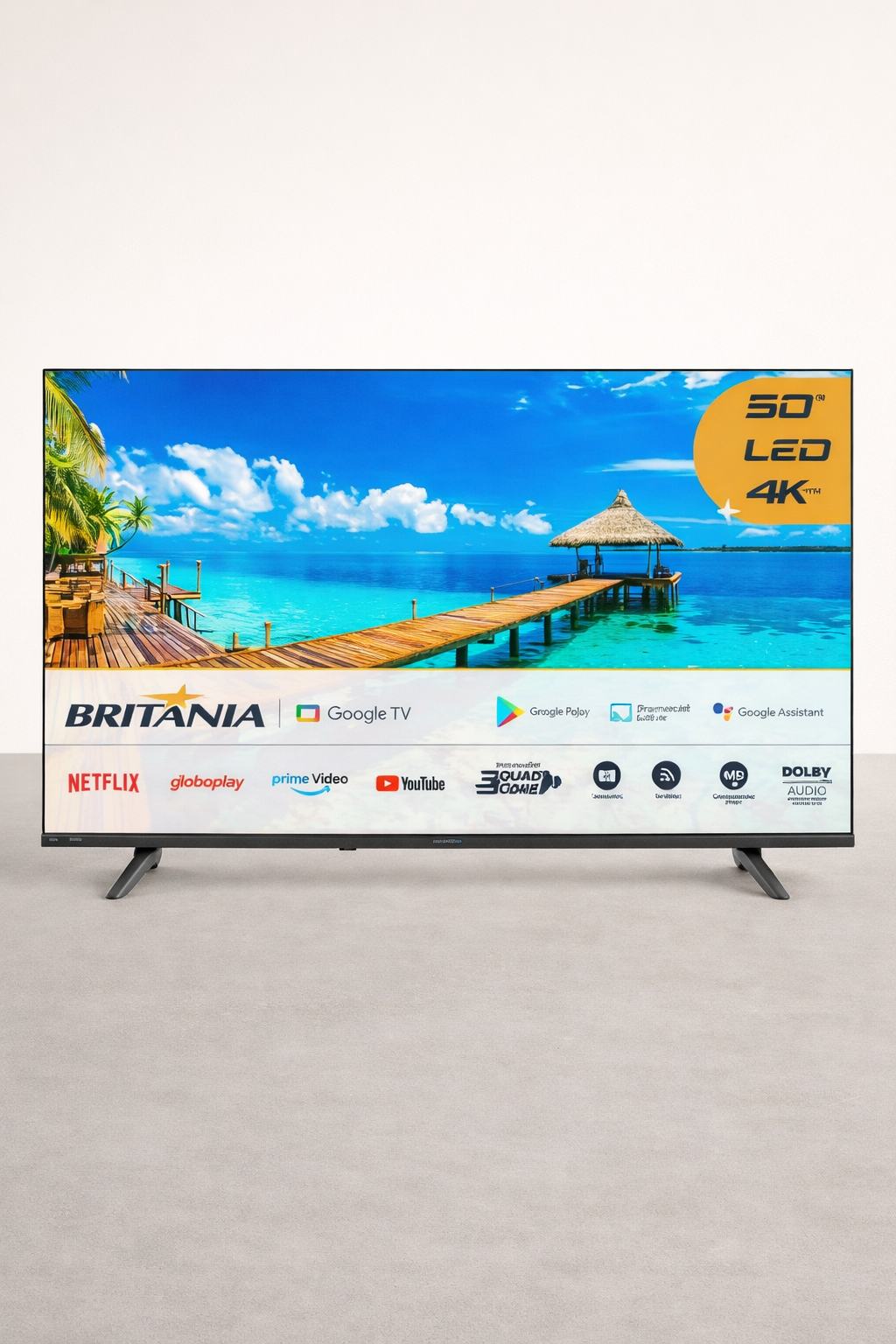 Televisor LED de 50 polegadas exibindo uma paisagem de praia com água azul e céu com nuvens, com logotipos de marcas como Britania, Google TV, Netflix e outros na parte inferior.
