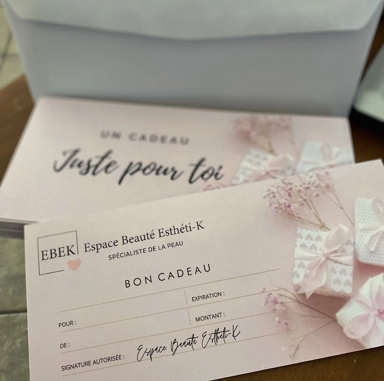 Une fiche cadeau rose avec des fleurs, des rubans, et des inscriptions en français. Elle appartient à un établissement appelé Espace Beauté Esthéli-K, et comporte des champs à remplir comme la validité, le montant, le nom de la personne offrant, et une signature.