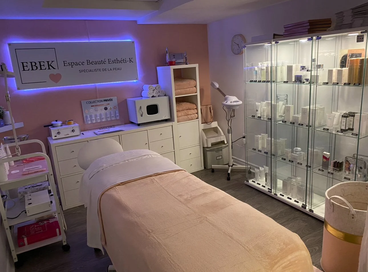 Salle de soins esthétiques avec un lit, une vitrine contenant des produits de beauté, et divers équipements de soins sur des étagères, dans un institut de beauté.