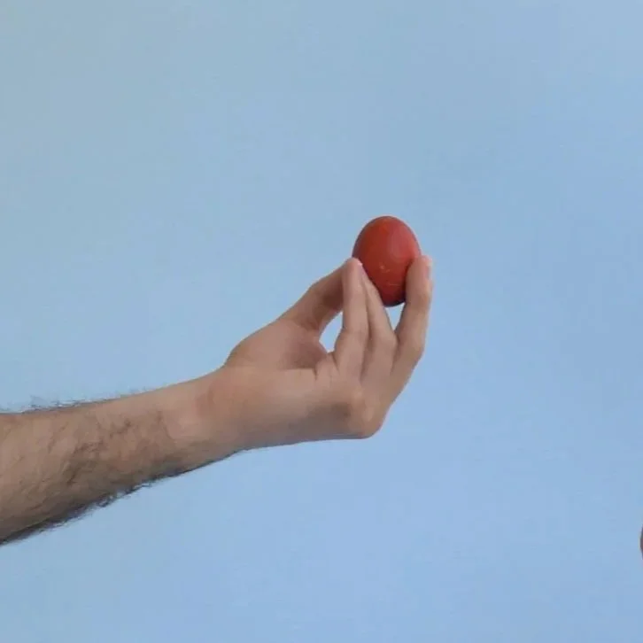 A person’s hand holding a red ball against a light blue background.
