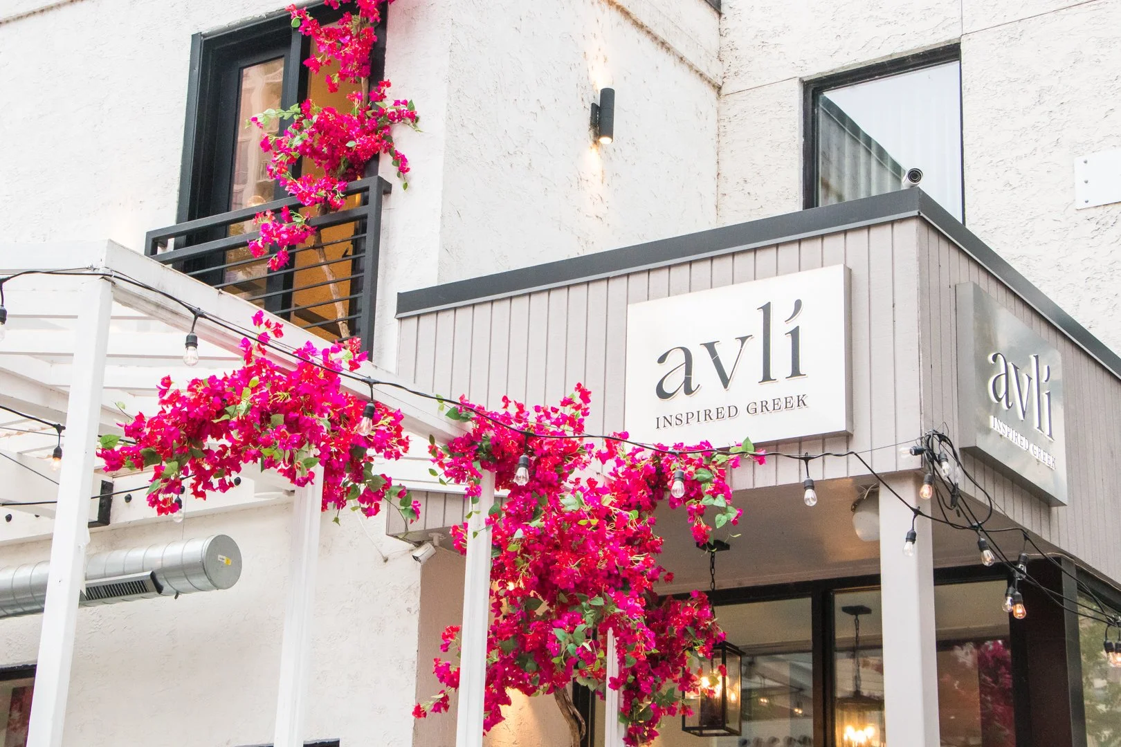 Exterior of a Greek-inspired restaurant called 'avli' with pink bougainvillea flowers and string lights