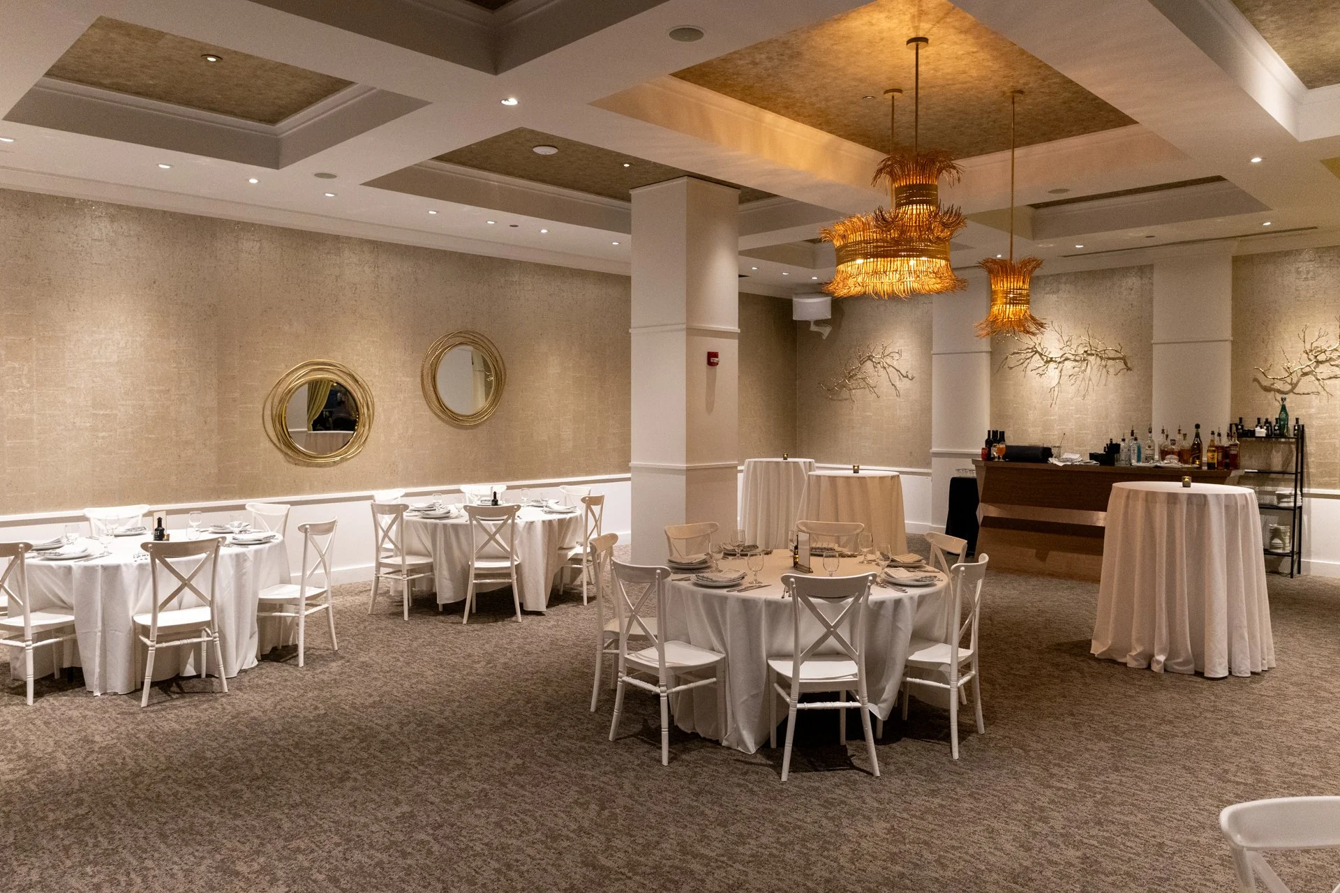 Elegant banquet hall decorated for a wedding or event with white tables, chairs, floral centerpieces, and warm lighting.