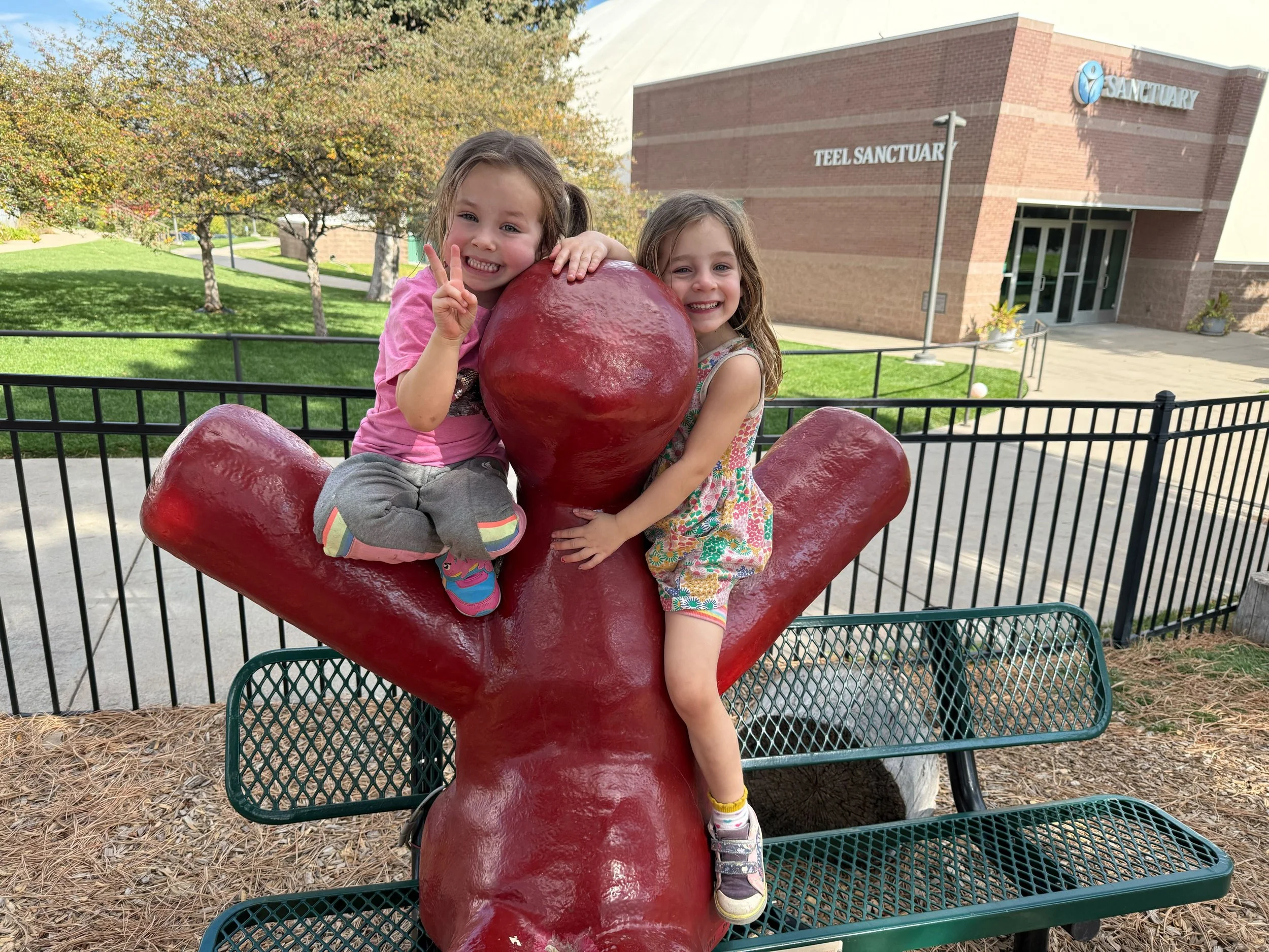 Two smiling girls sit on a statue, one is holding up a peace sign