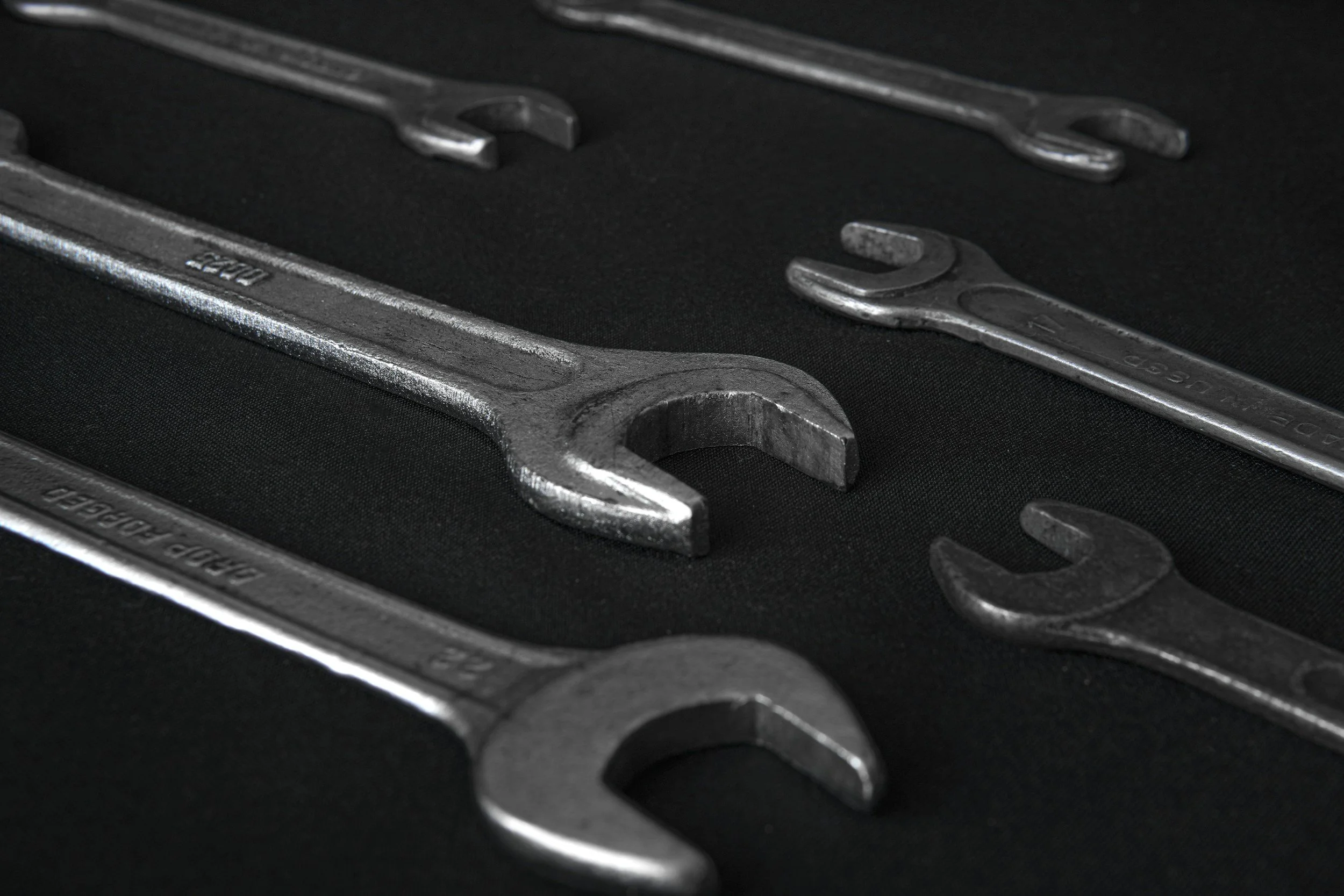 A set of metal wrenches of various sizes on a black background.