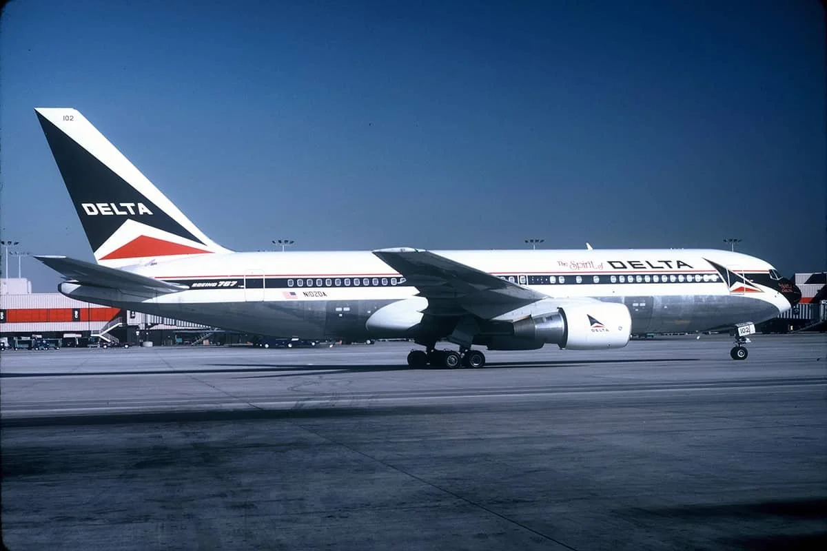 A Delta Airlines Boeing 767 airplane parked on the tarmac at an airport. The plane has a white body with the Delta logo on the tail and the name 'The Spirit of Delta' written on it.