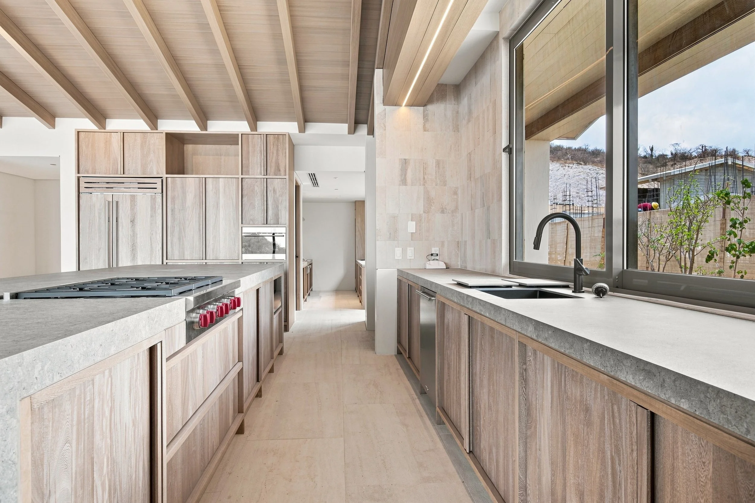 Modern kitchen with wooden cabinets and countertops, large window overlooking a hillside with a house and trees.
