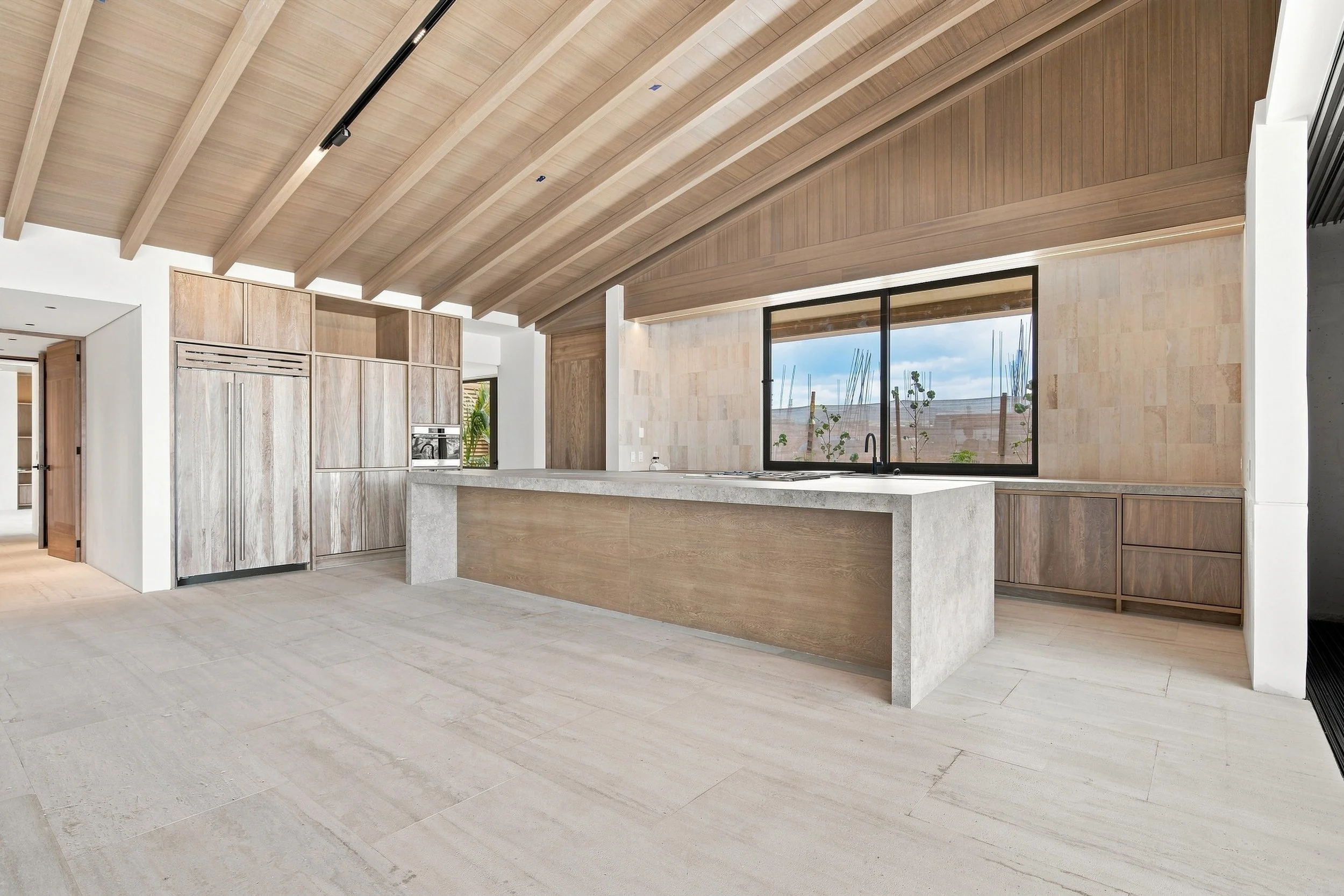 Modern kitchen with wood-paneled vaulted ceiling, large window, and light-colored tile flooring.