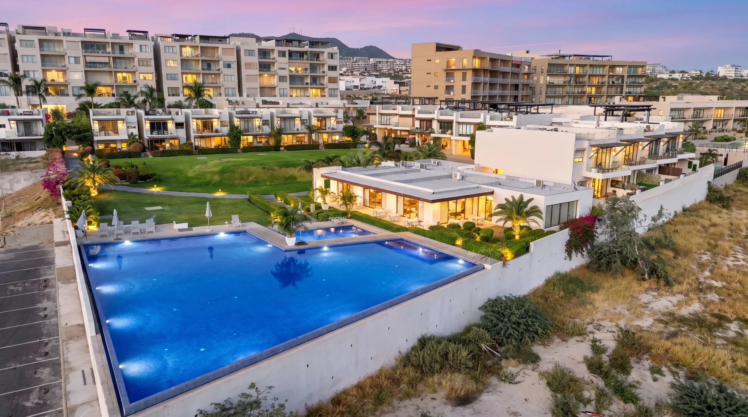 A luxurious apartment complex featuring multiple buildings, a large swimming pool, and surrounding landscaped gardens at dusk at Vista Vela 