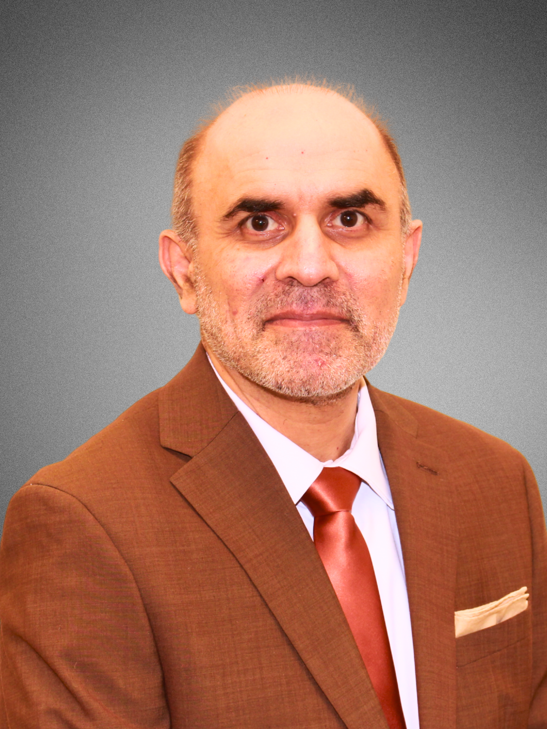 A middle-aged man with a beard and mustache, wearing a dark suit, black shirt, and red tie, posing against a plain background.